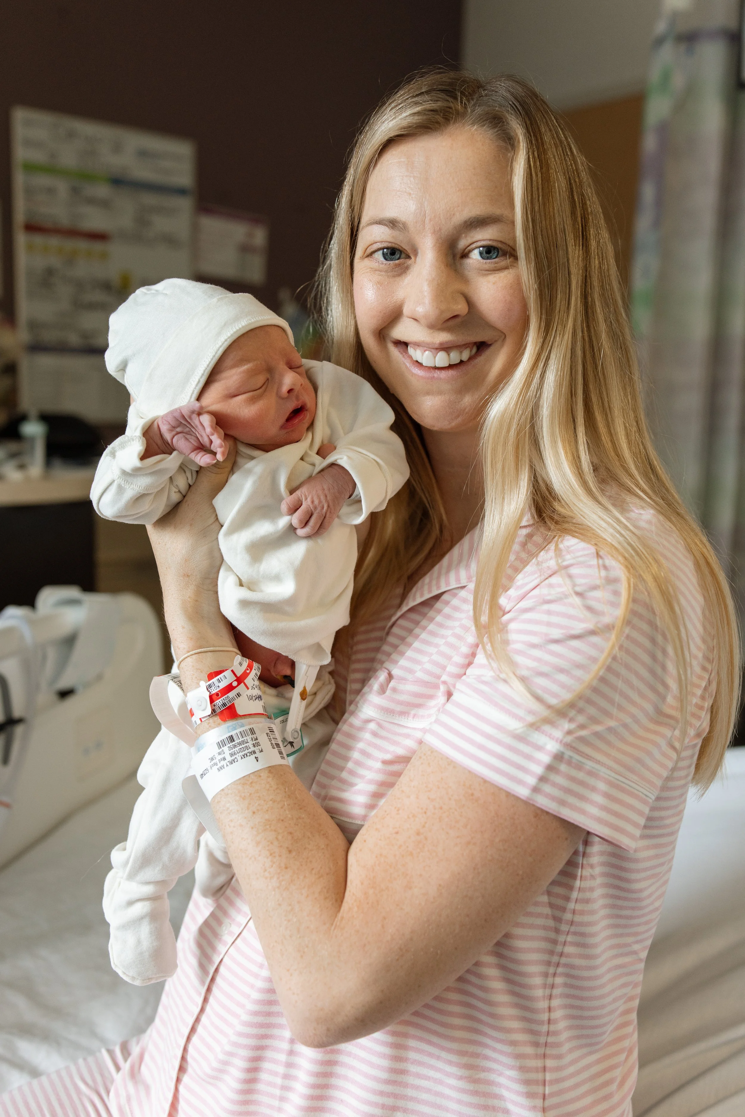 A woman in a pink striped hospital gown holding a newborn baby in a hospital room. fresh 48 photography Austin Texas