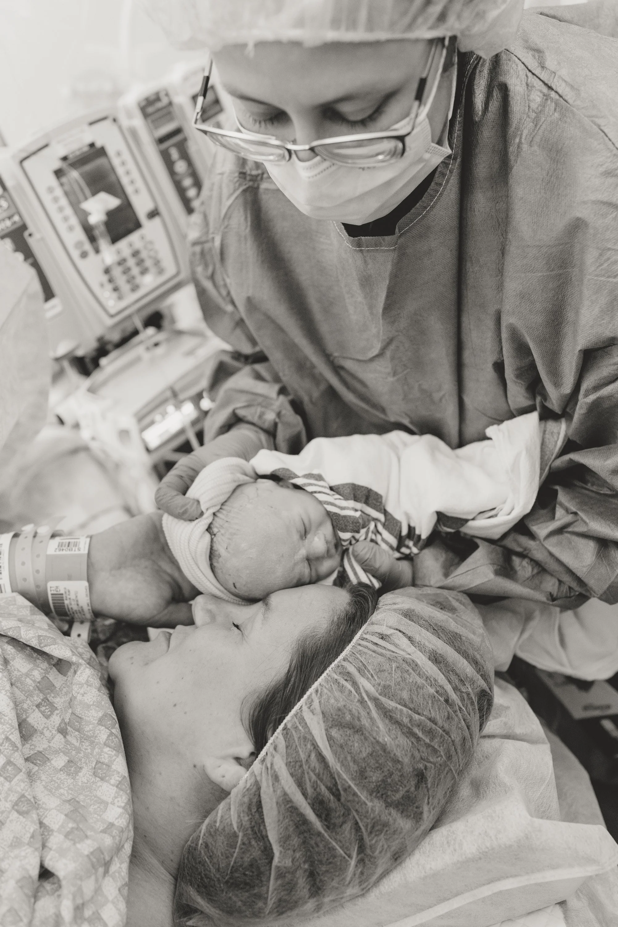 A woman in hospital attire cradles her newborn baby in her arms, both with eyes closed, in a moment of bonding after childbirth. c-section birth photographer in Austin Texas