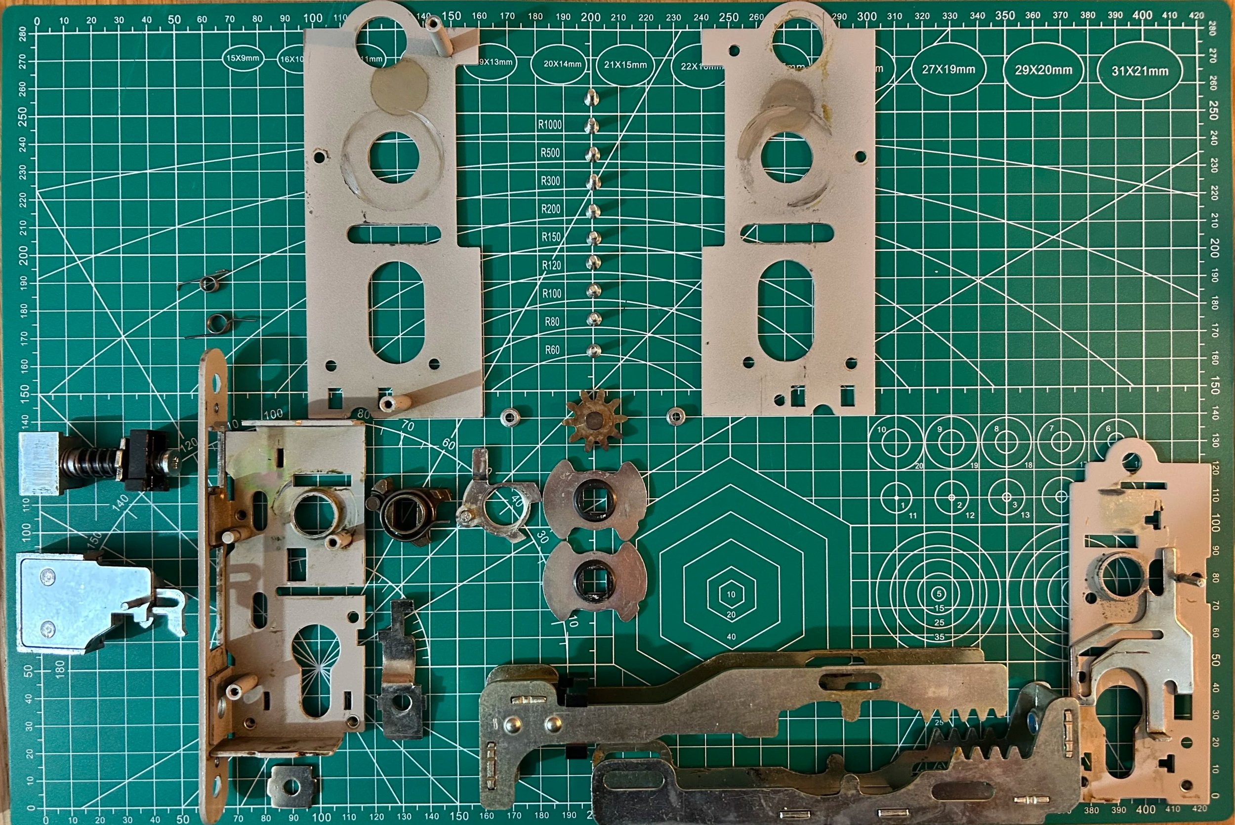 An overhead view of disassembled mechanical  parts arranged on a green cutting mat with measurement markings. Everest 3 point locking mechanism from 1972 getting repaired.