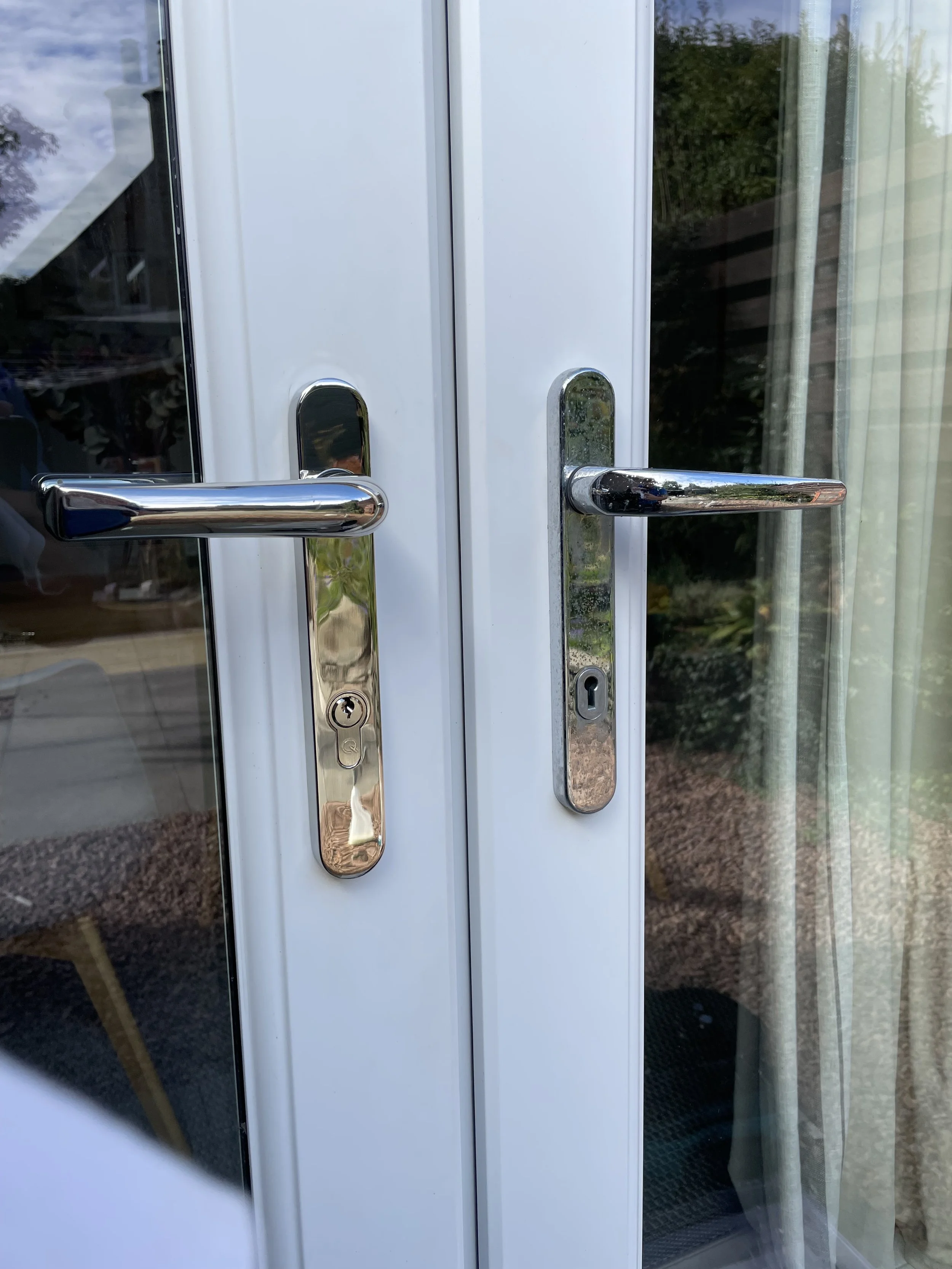 Close-up of glass door with gold-colored handles and locks, view of outdoors through reflection, and a curtain on the right side. new handles. new locks. Mila handles
