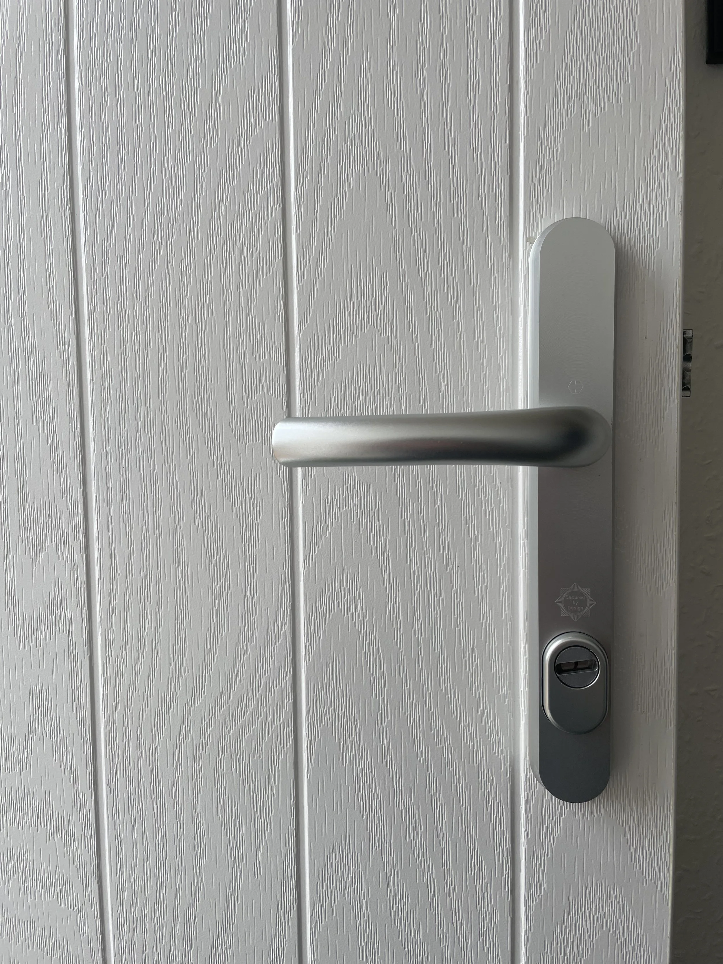 Close-up of a white textured door with a horizontal silver door handle and a lock below it.