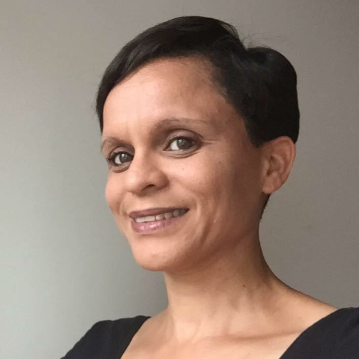 Close-up of a woman with short dark hair, wearing a black top, smiling against a plain background.