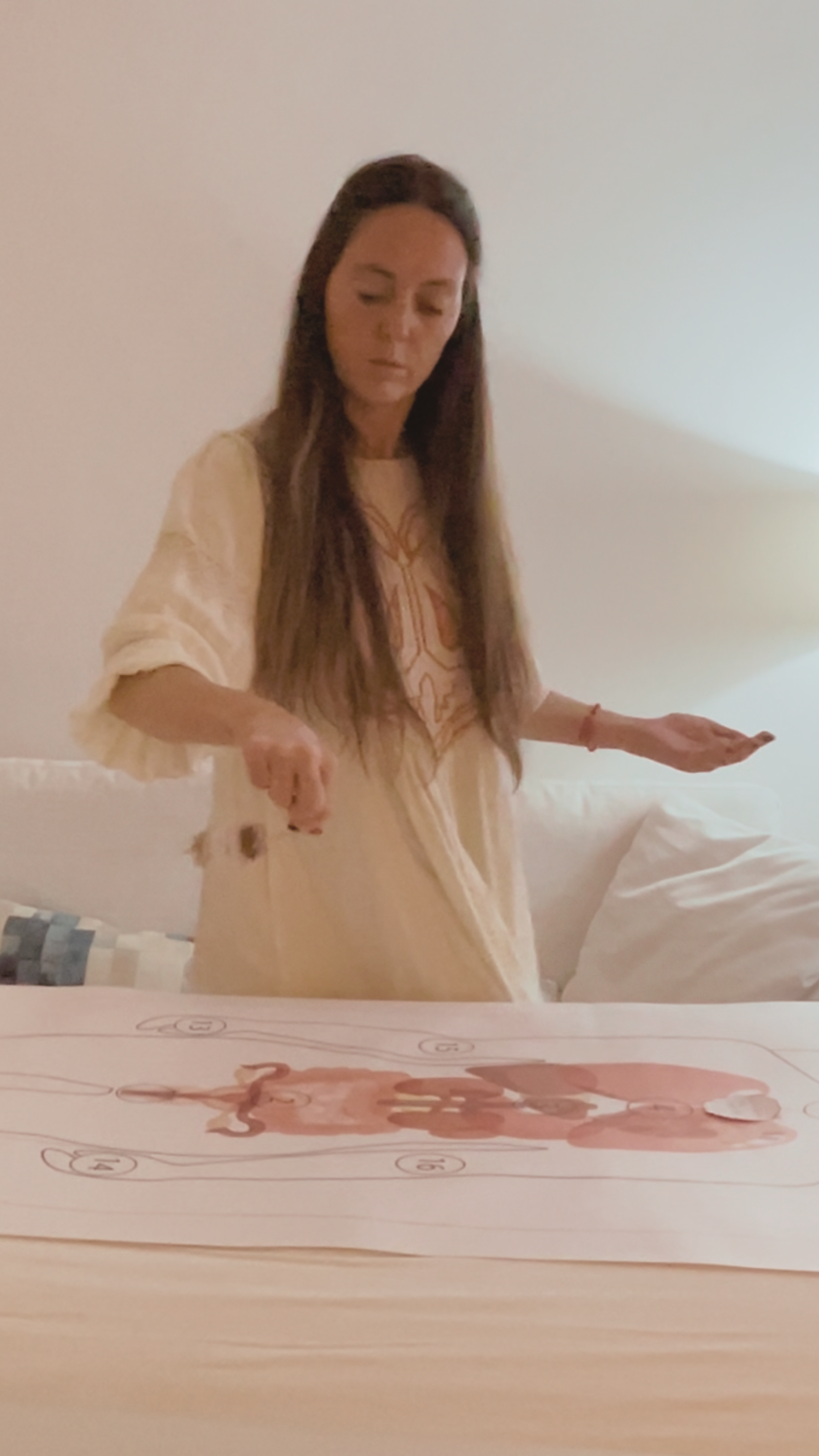 Una donna con capelli lunghi e occhi chiusi, indossa un abito beige con disegni geometrici e si trova in una stanza con pareti chiare. Sta facendo una sessione con il pendulo ebraico.