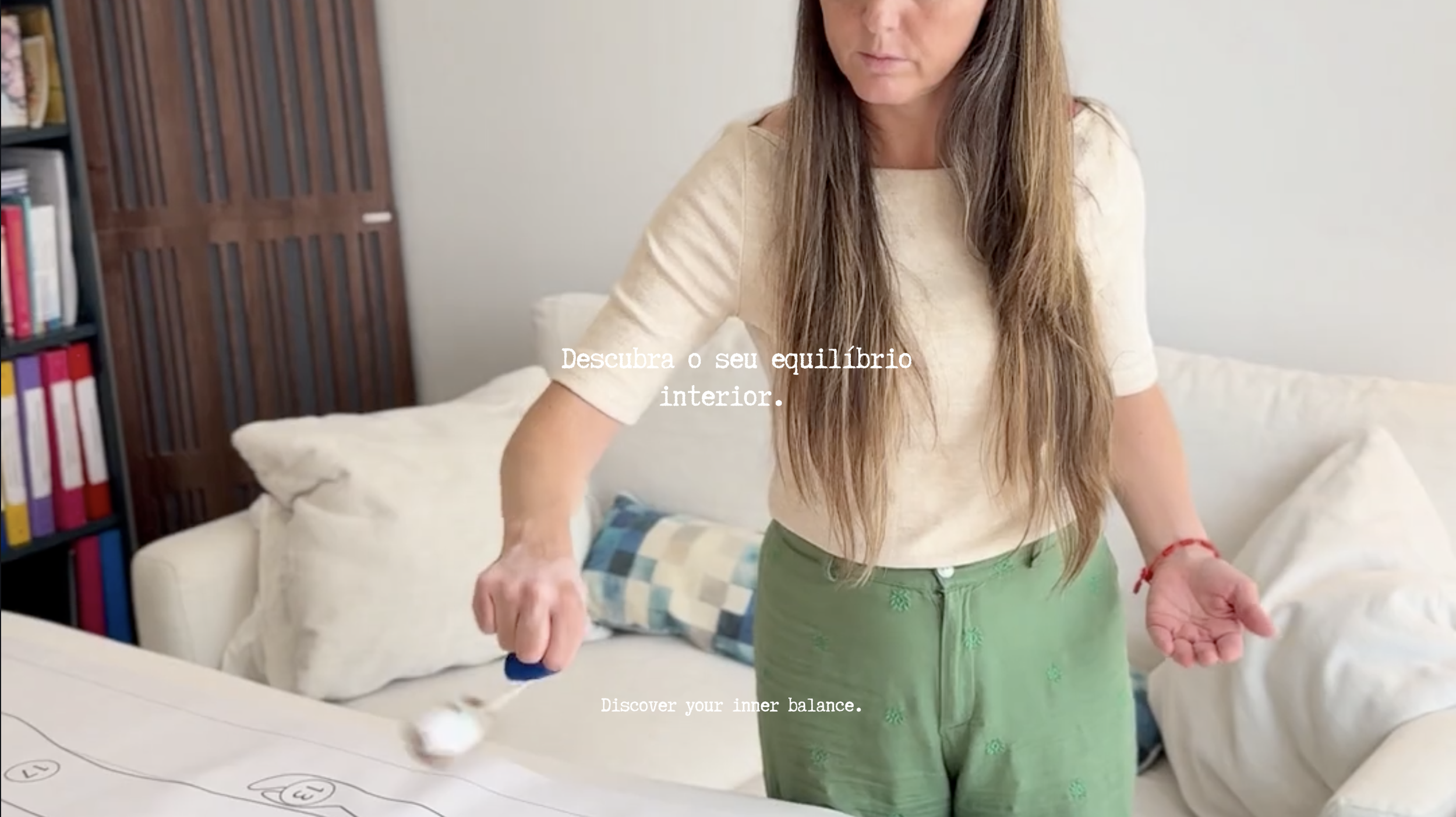 Una donna con lunghi capelli castani indossa una maglietta beige e pantaloncini verdi mentre si trova in una stanza,lavorando con il pendulo ebraico con un testo sovrapposto in italiano e inglese che invita a scoprire il proprio equilibrio interiore.