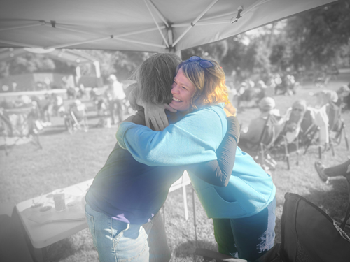 Two women hugging and smiling at an outdoor event or fair.