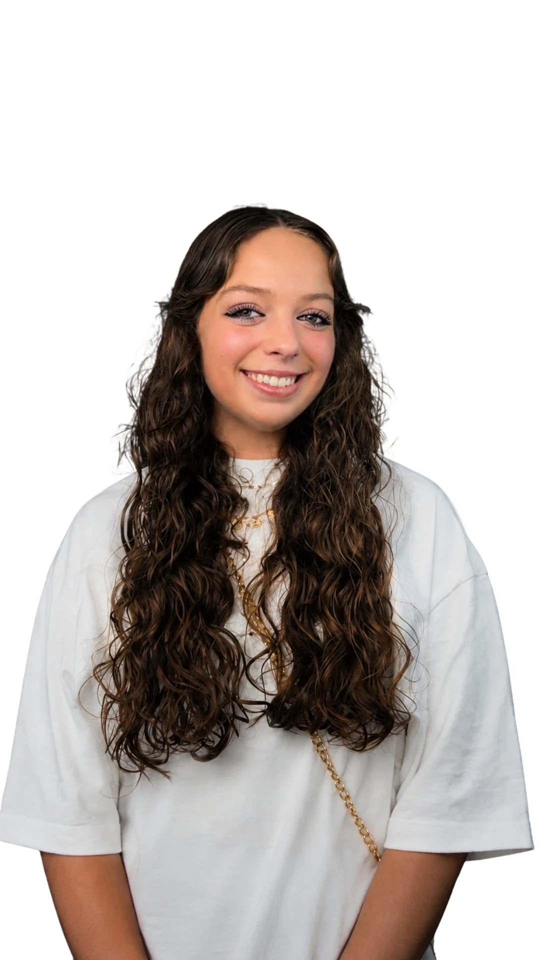 Jeune femme avec longs cheveux bouclés, sourire, portant un t-shirt blanc et une chaîne dorée, fond blanc.