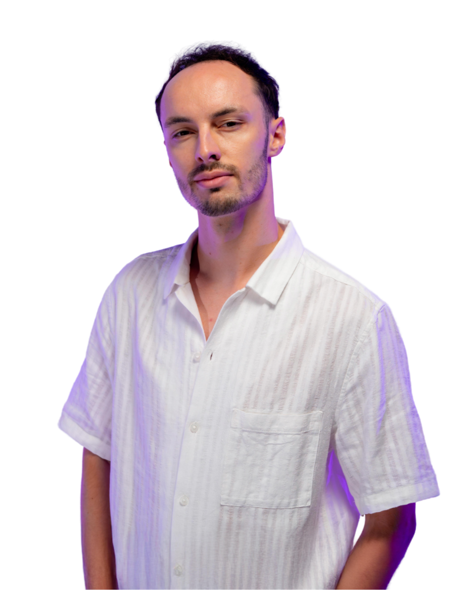 Un jeune homme avec une barbe, portant une chemise blanche à rayures, pose contre un fond blanc avec une lumière violette