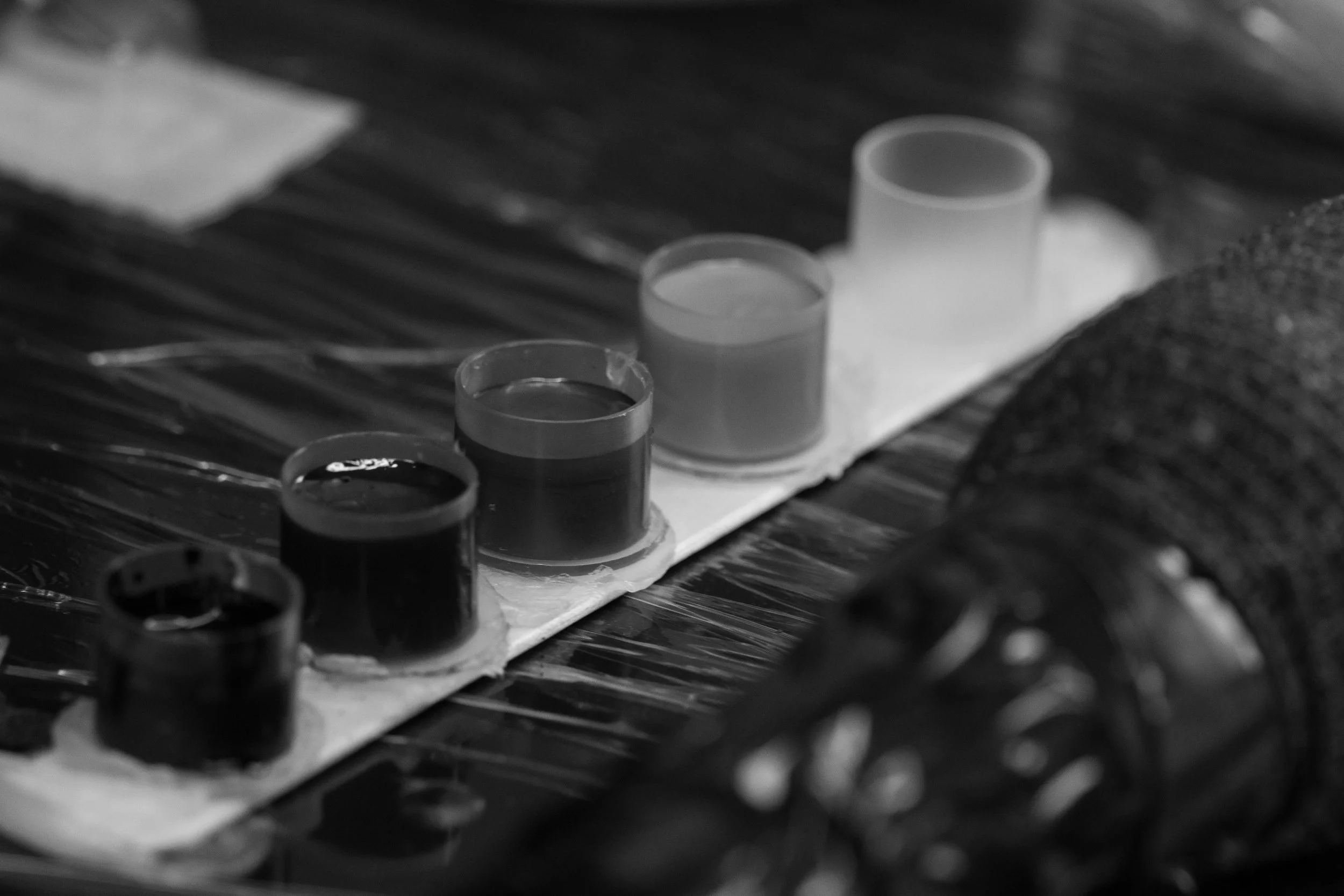 Black and white photo of several test tubes filled with liquids placed on a piece of paper on a textured surface.
