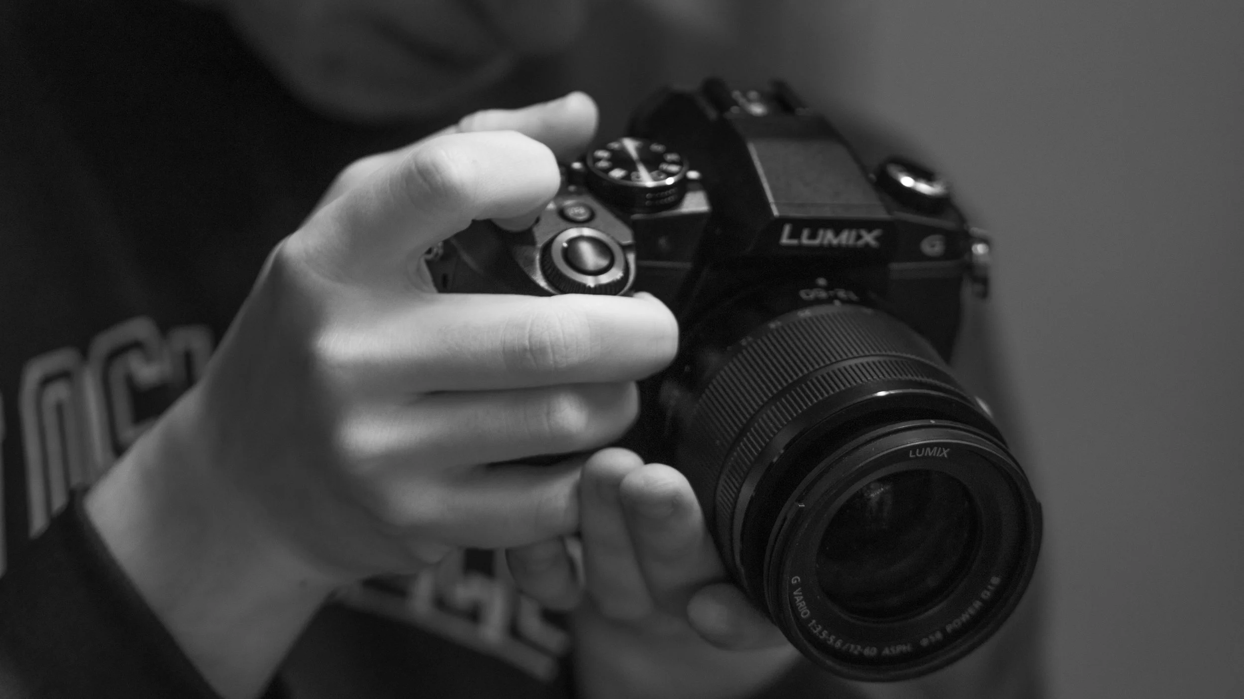 Black and white photo of a person's hand holding a Panasonic Lumix digital camera, with a blurred background.