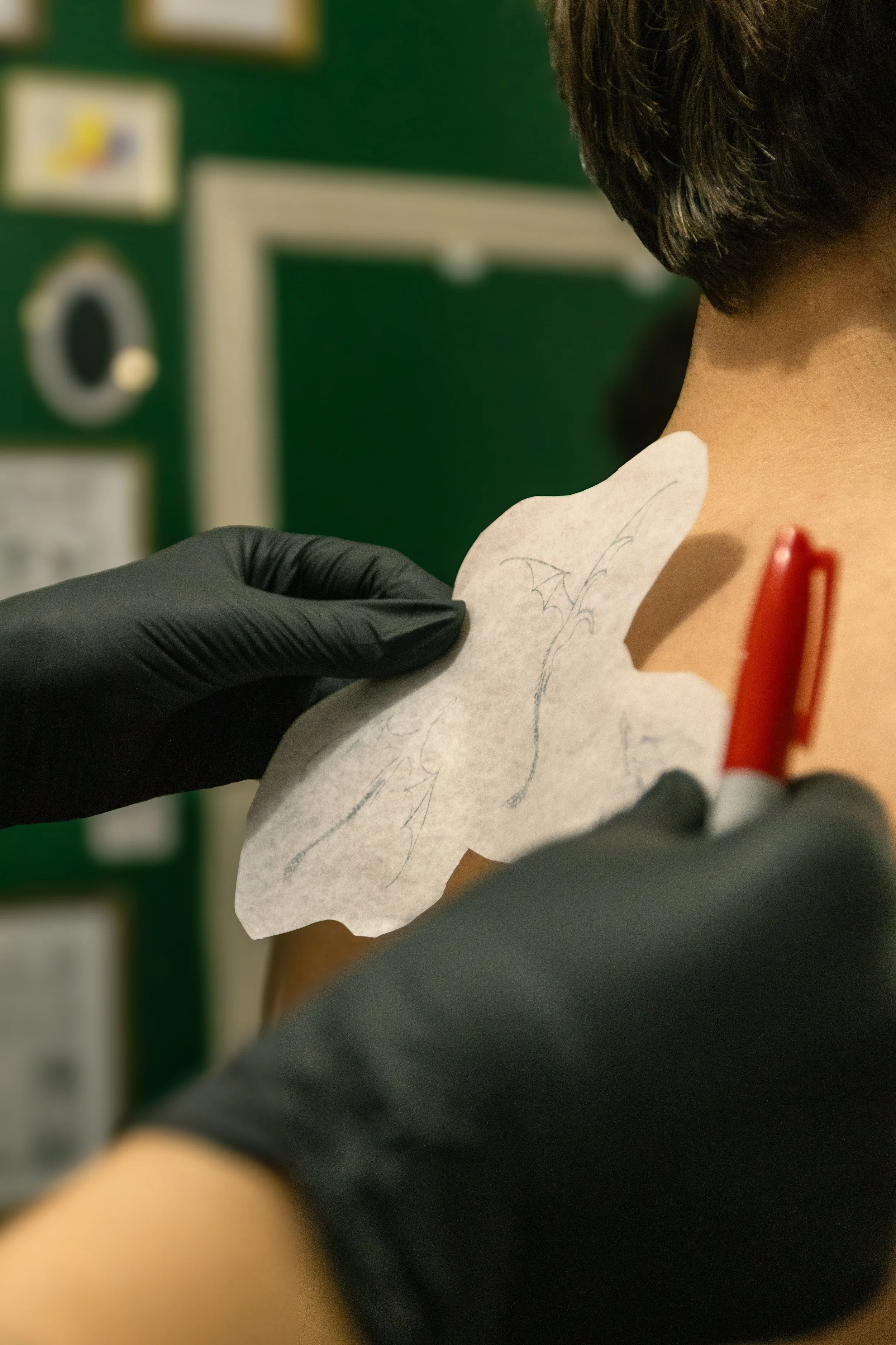 A person receiving a tattoo of a bat on their shoulder from a tattoo artist wearing black gloves.