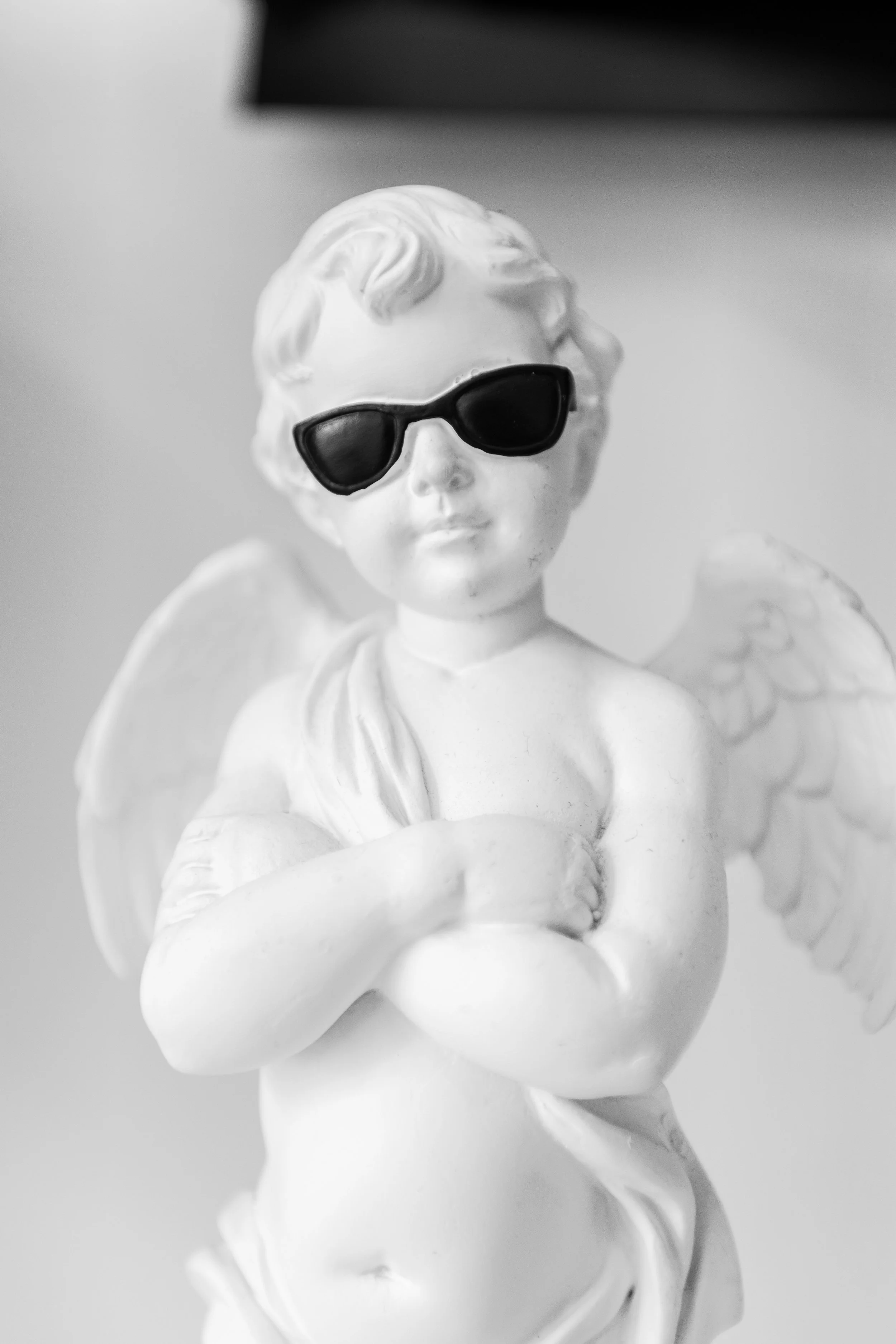 A white angel figurine wearing black sunglasses, holding a baby angel in its arms.