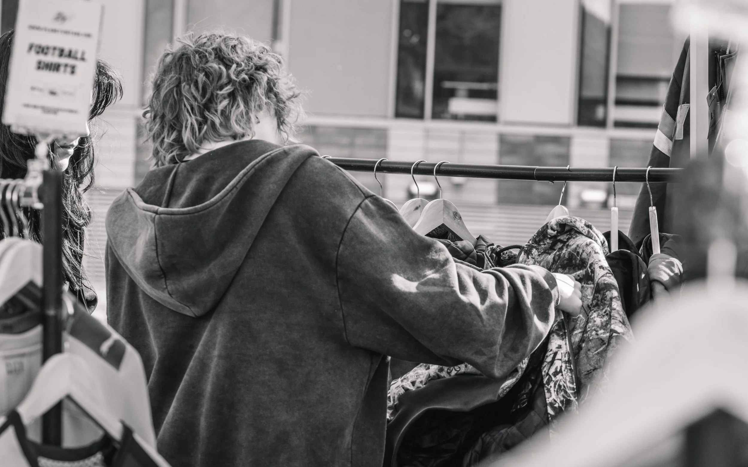 A person with curly hair shopping for clothes at a store, browsing items on a rack.