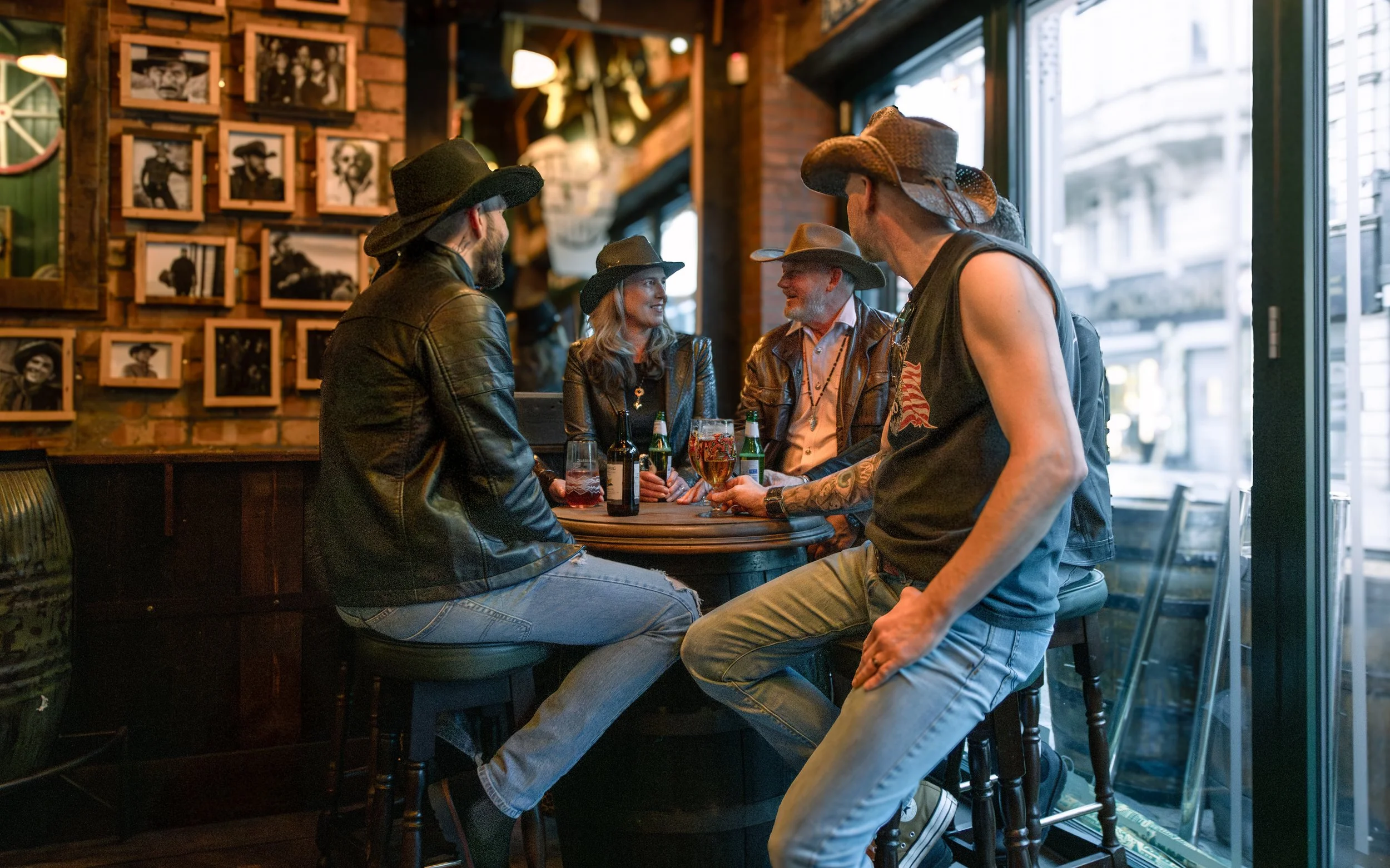 A group of five people in a bar, wearing cowboy hats, talking and drinking beer and wine.