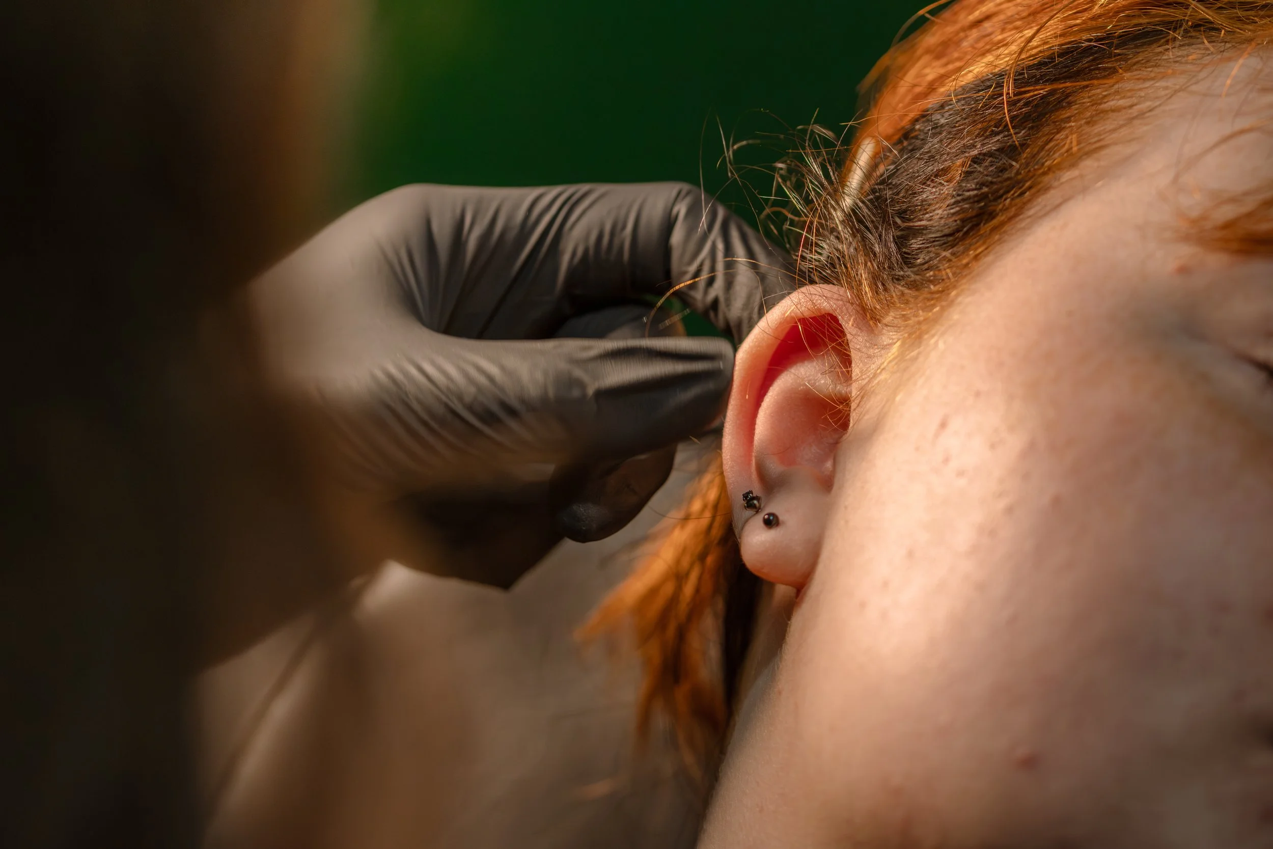 Close-up of a person's ear with piercings, with a gloved hand inserting an earring.