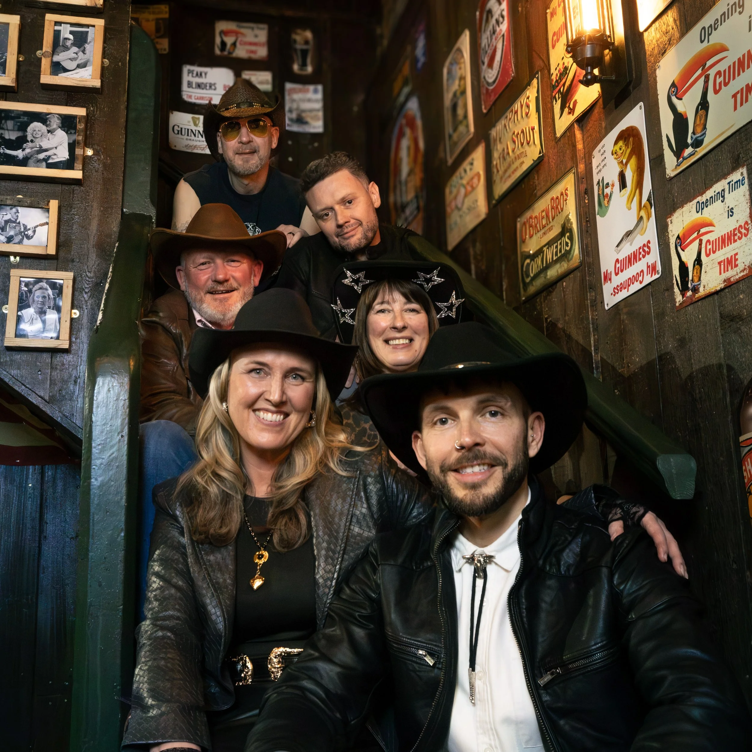 Group of people sitting closely together in a dimly lit, vintage-themed bar with posters and photographs on the walls.