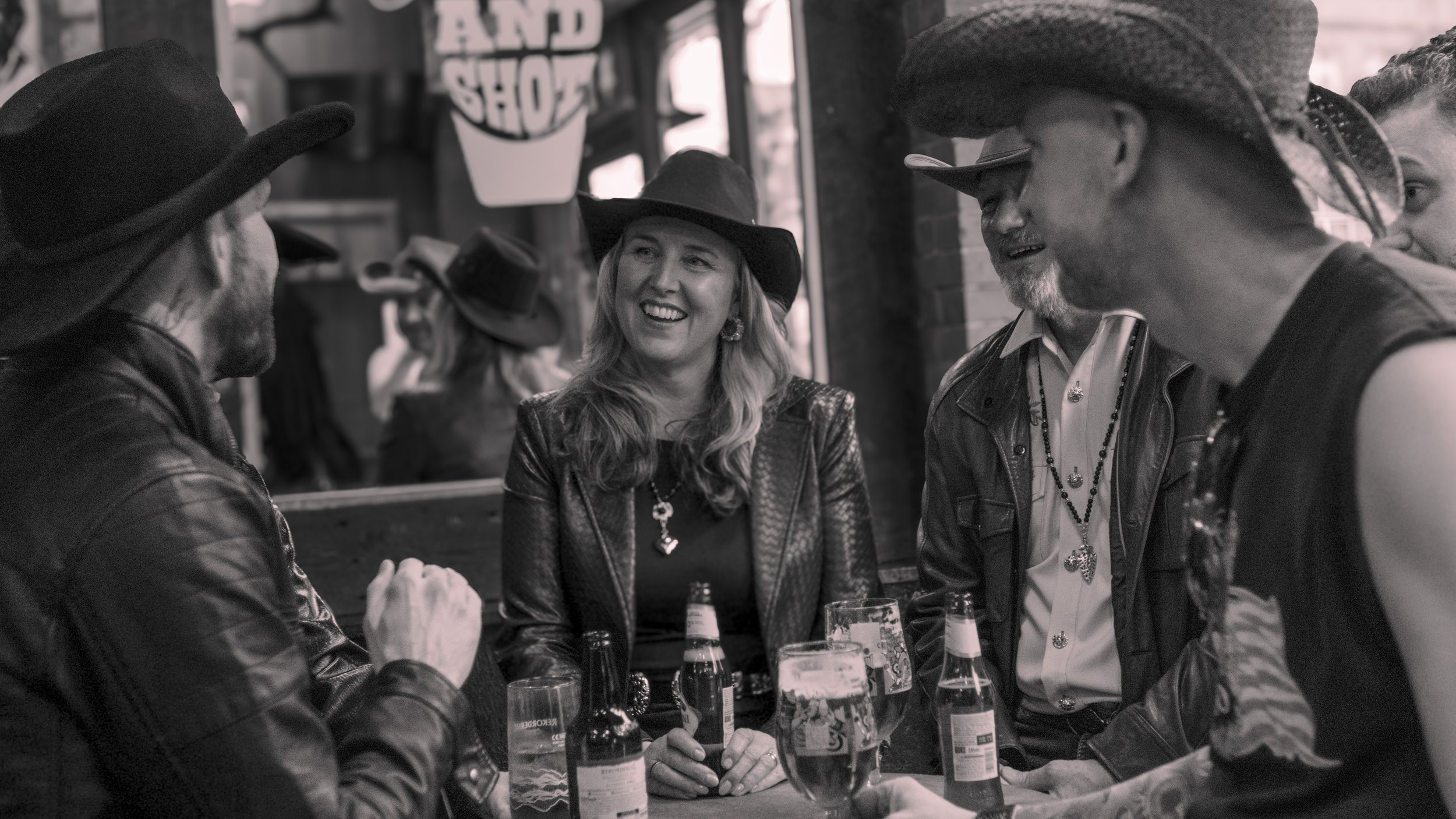 Group of friends wearing cowboy hats socializing at a bar with bottles and glasses on the table.
