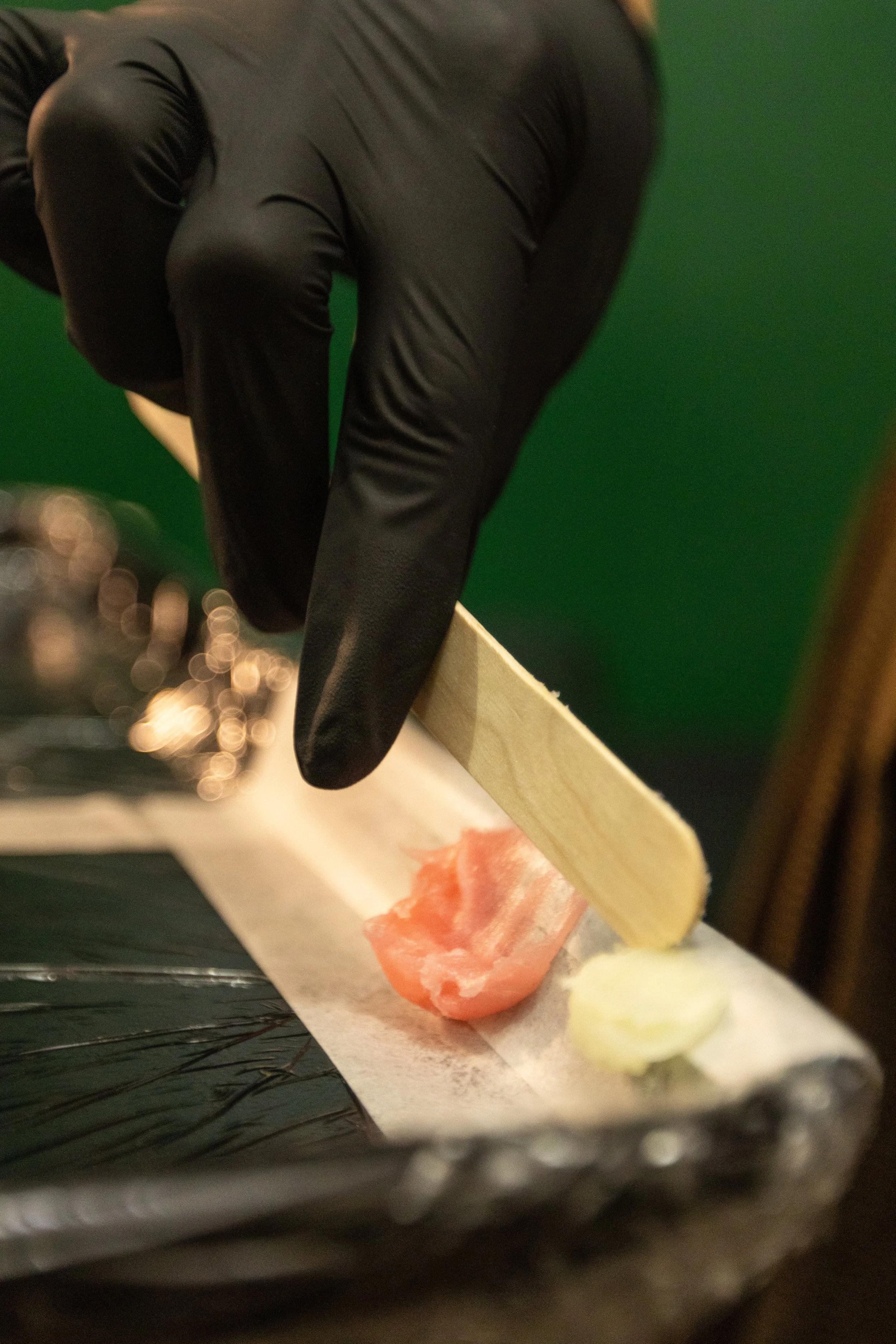 Close-up of a sushi roll with raw salmon, wrapped in nori with rice, accompanied by slices of ginger and wasabi, on a sushi rolling mat.