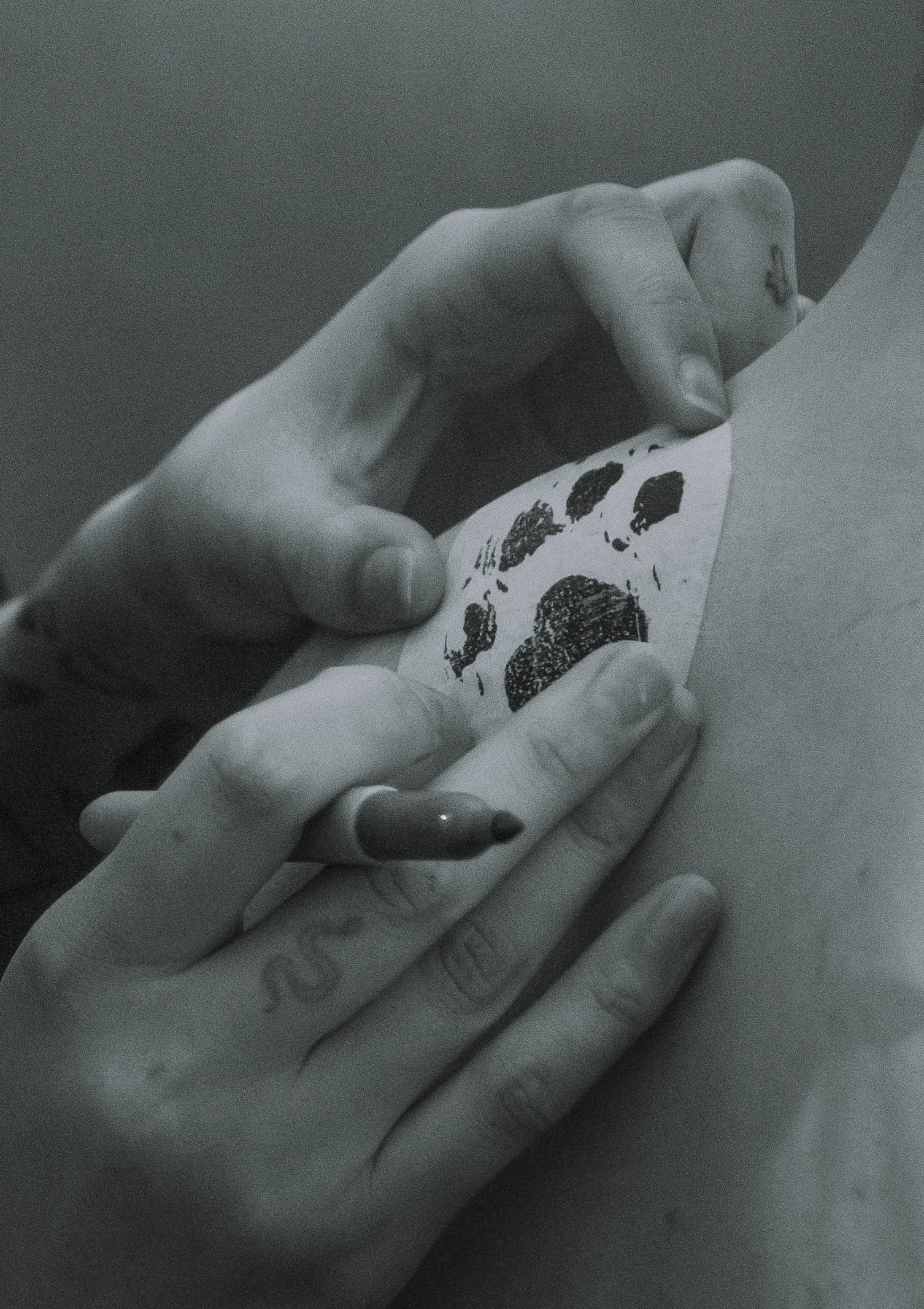 Close-up of a person's hand with painted nails, holding a piece of paper with black ink blot images.