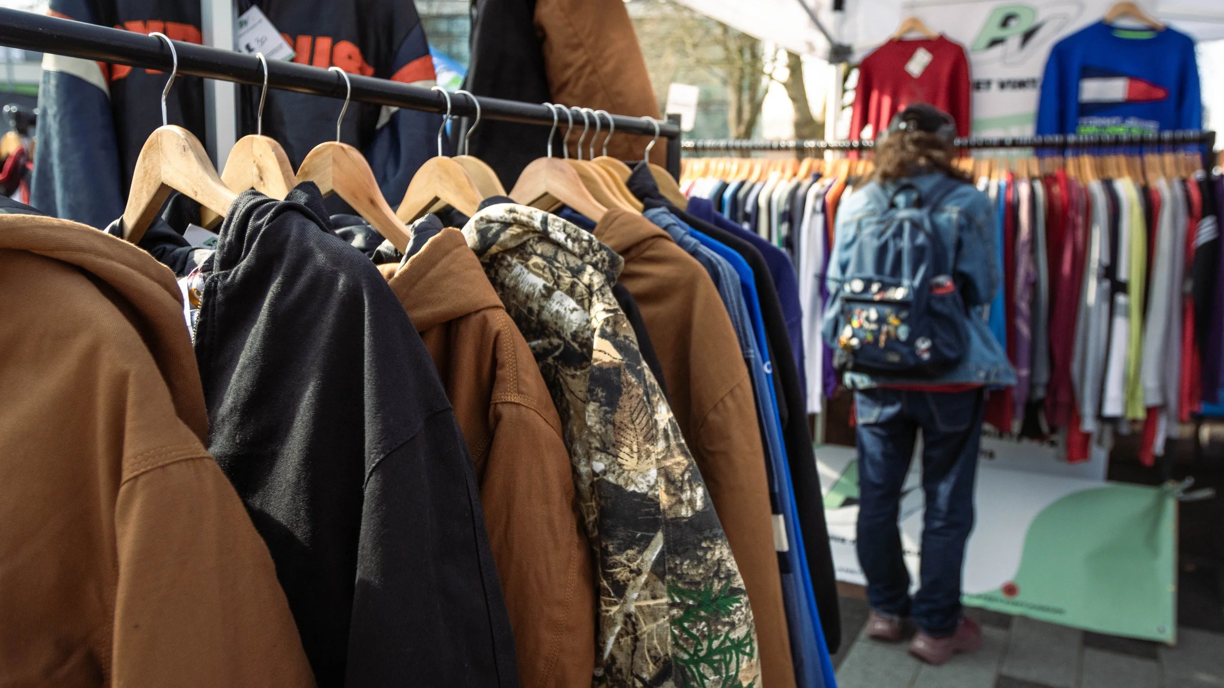 Clothing racks with various jackets and shirts at an outdoor market.