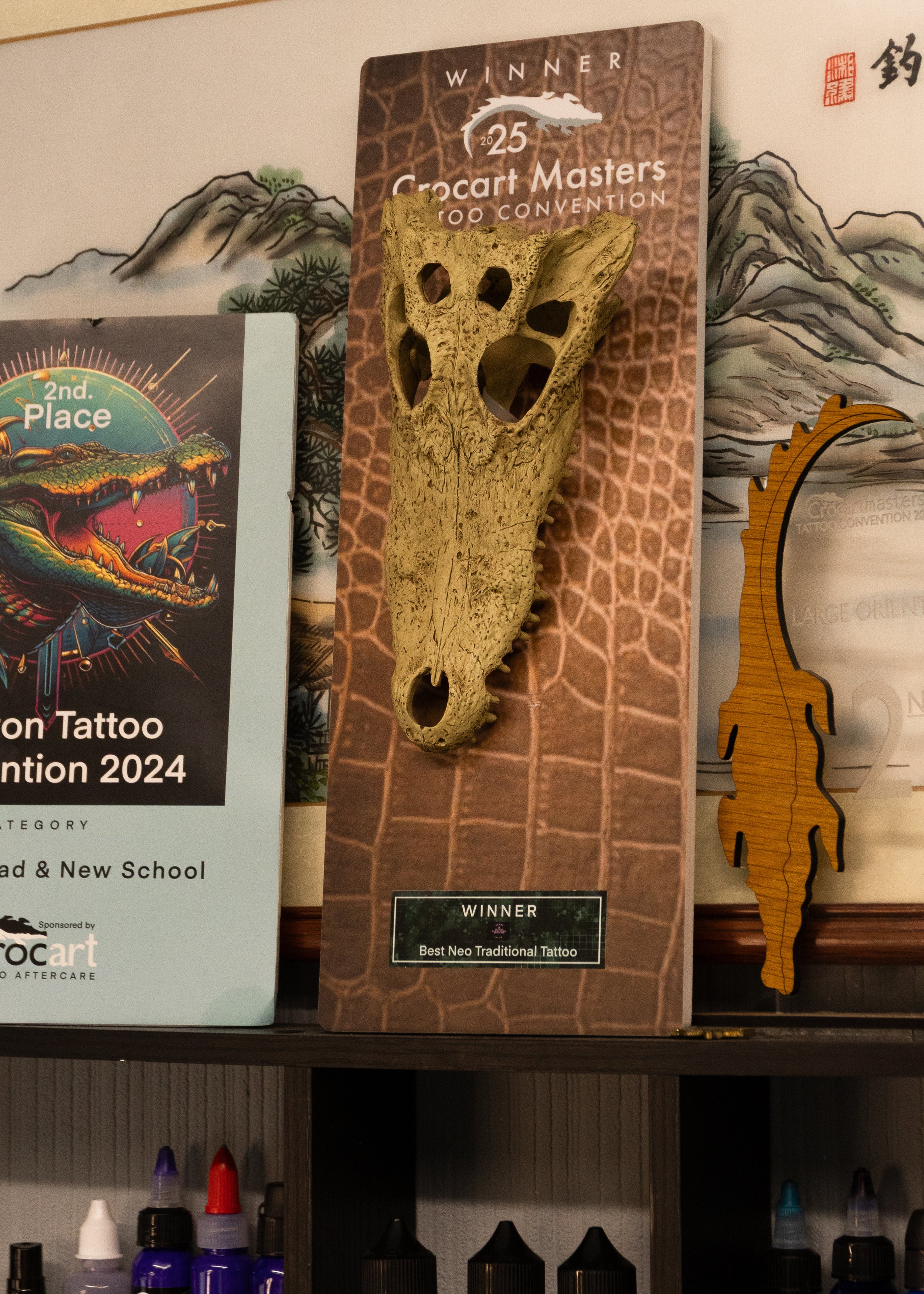 A wooden plaque with a carved animal skull, labeled as the winner of the 2025 Crocart Masters Tattoo Convention, Best Neo Traditional Tattoo, standing on a display board.