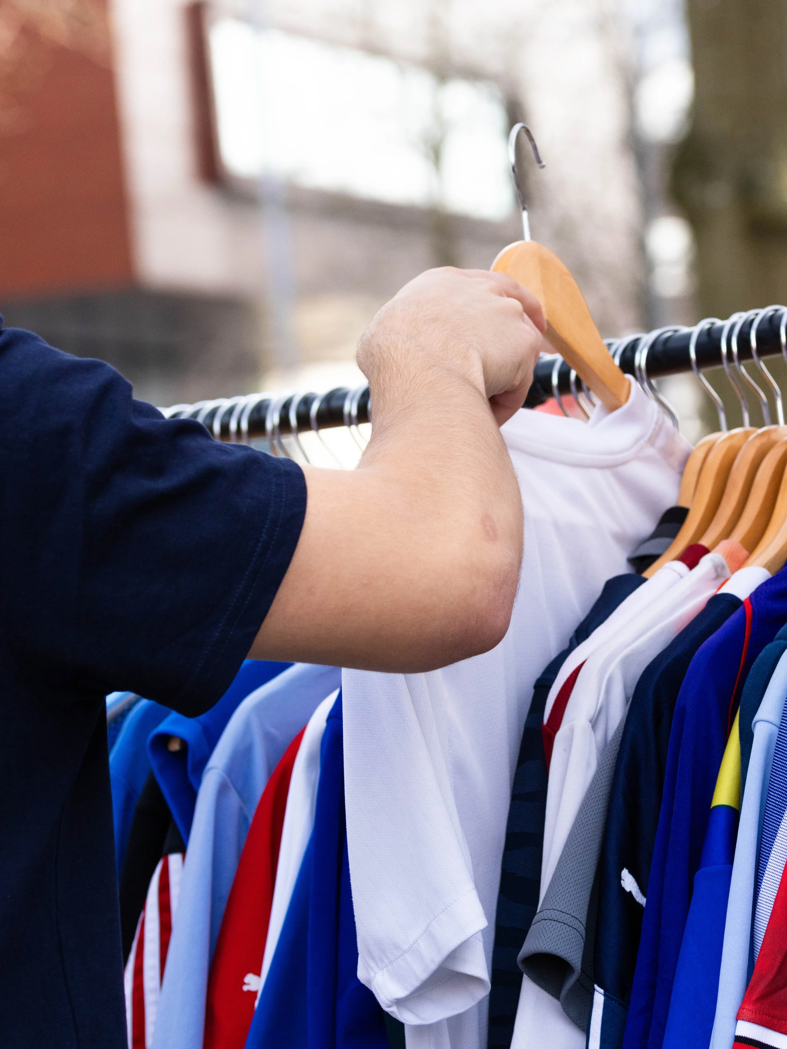 A person hanging colorful sports jerseys on a clothing rack outside.