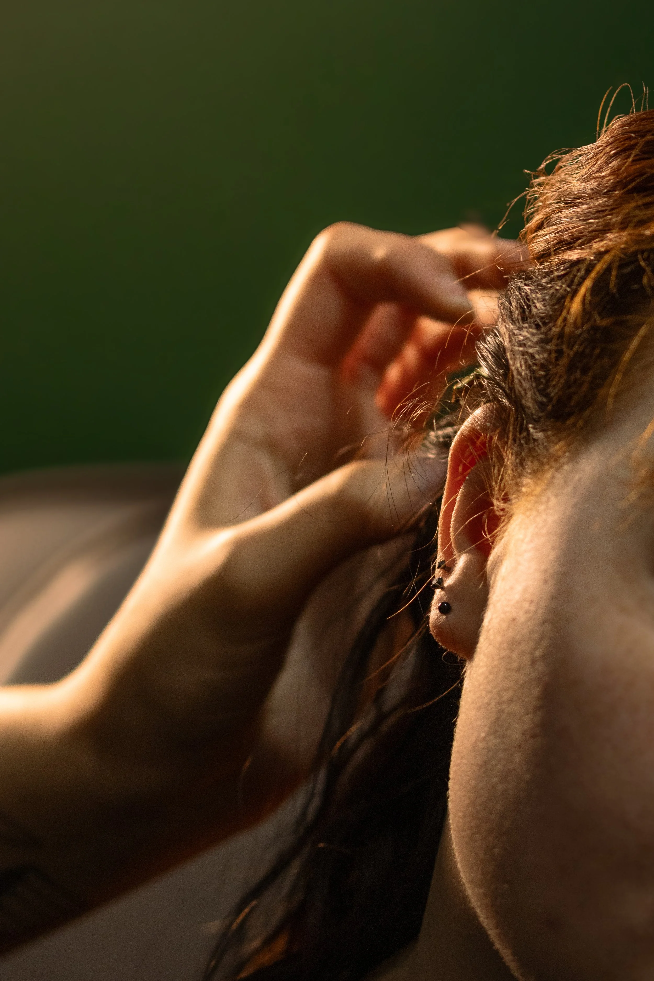 Close-up of a woman with brown hair and earrings, touching her hair with her hand