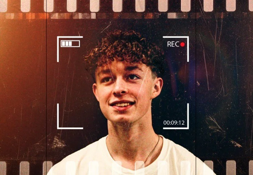 Young man with curly hair smiling at the camera during a video recording.