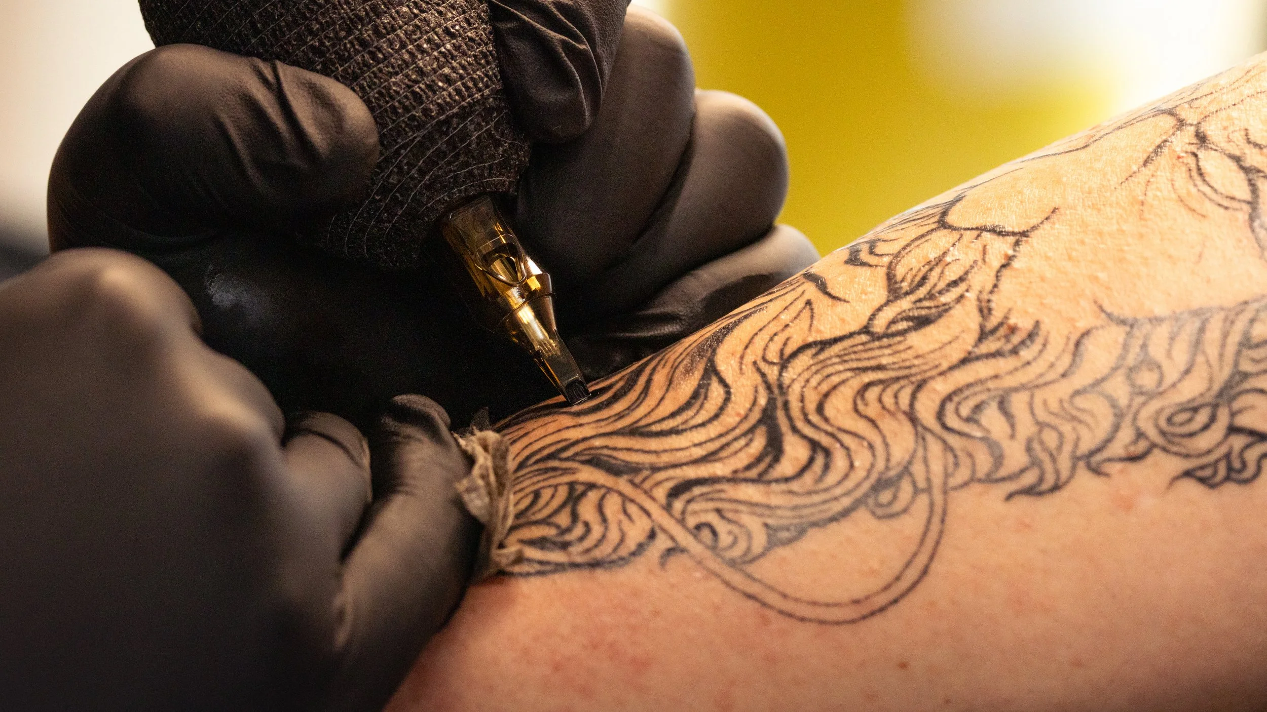 A tattoo artist using a tattoo machine to ink a detailed, black line design onto a person's skin.