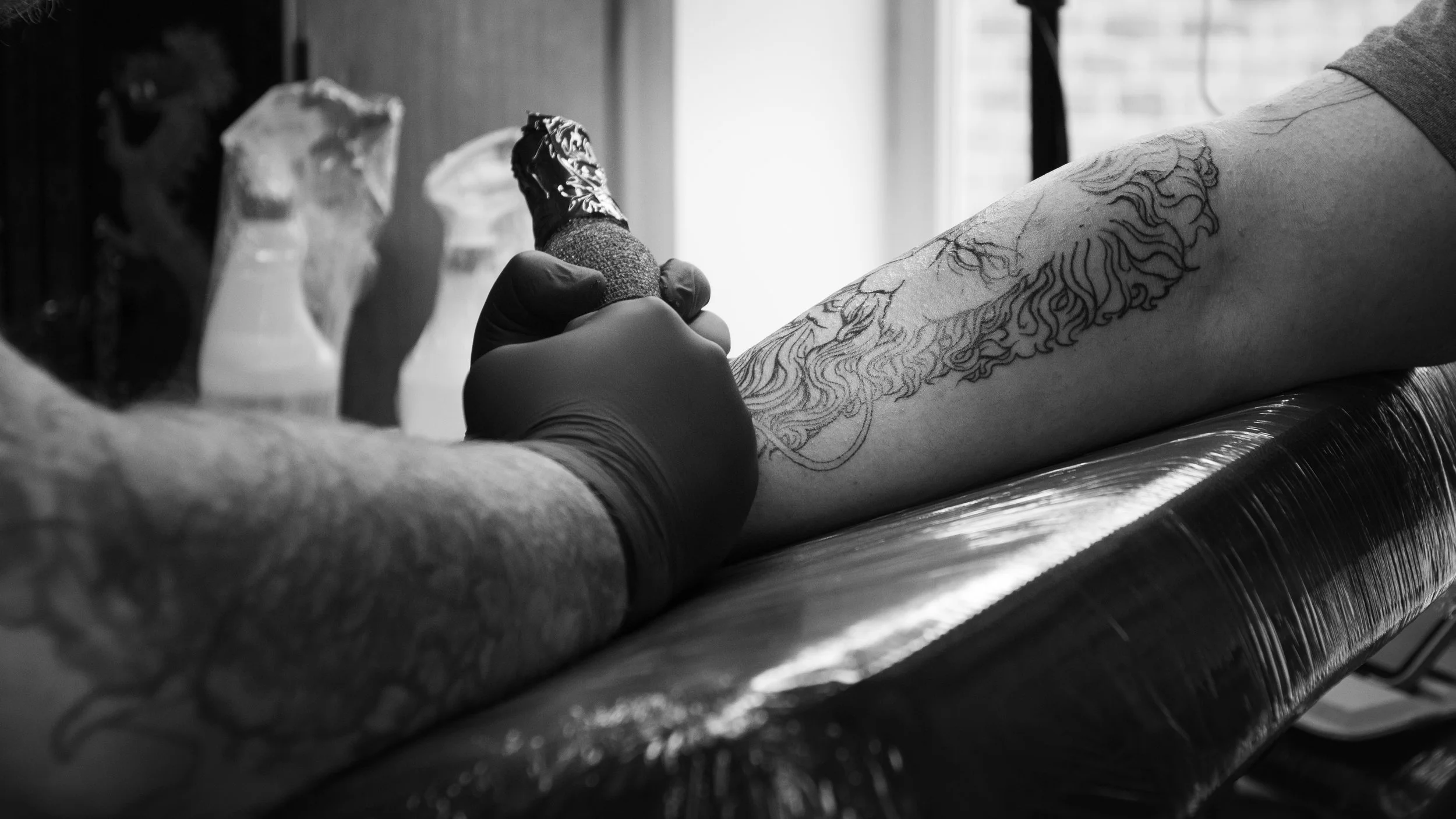 A person with a tattoo on their arm getting a tattoo on their forearm in a tattoo studio.