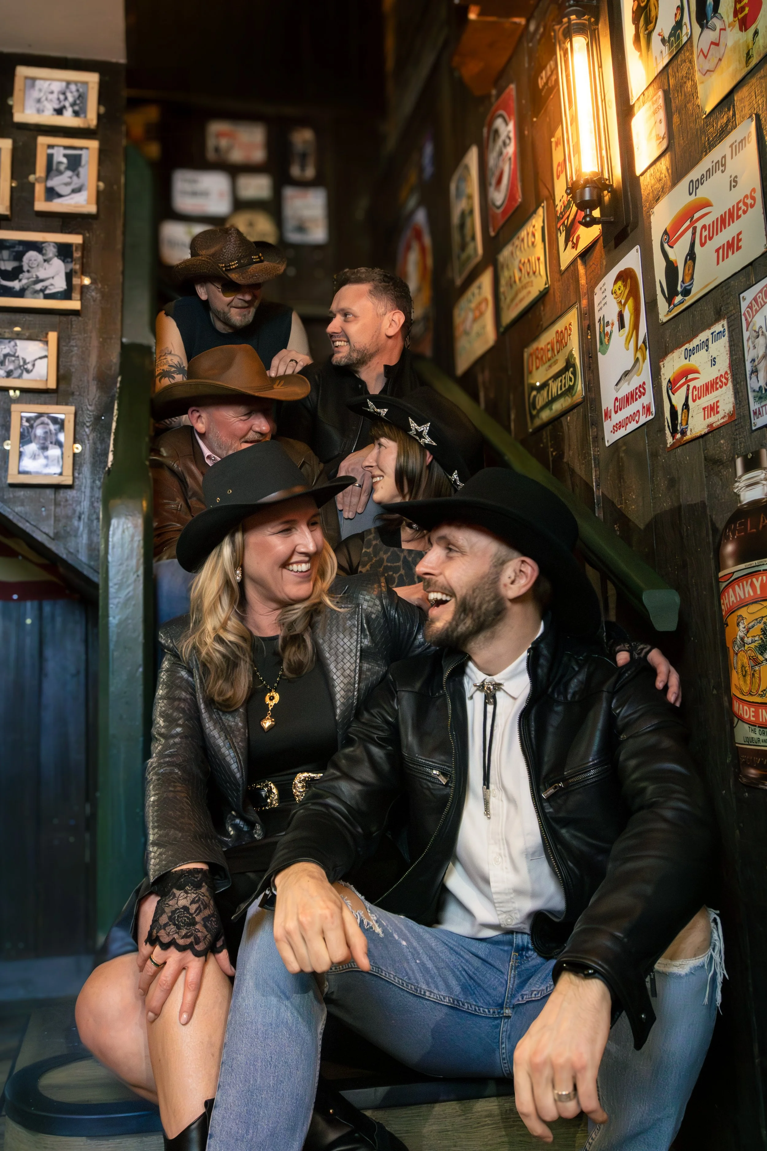 A group of people enjoying themselves in a cozy, vintage-style bar with retro signs on the wall. They are smiling, laughing, and engaged in conversation, dressed in casual and country-inspired clothing.