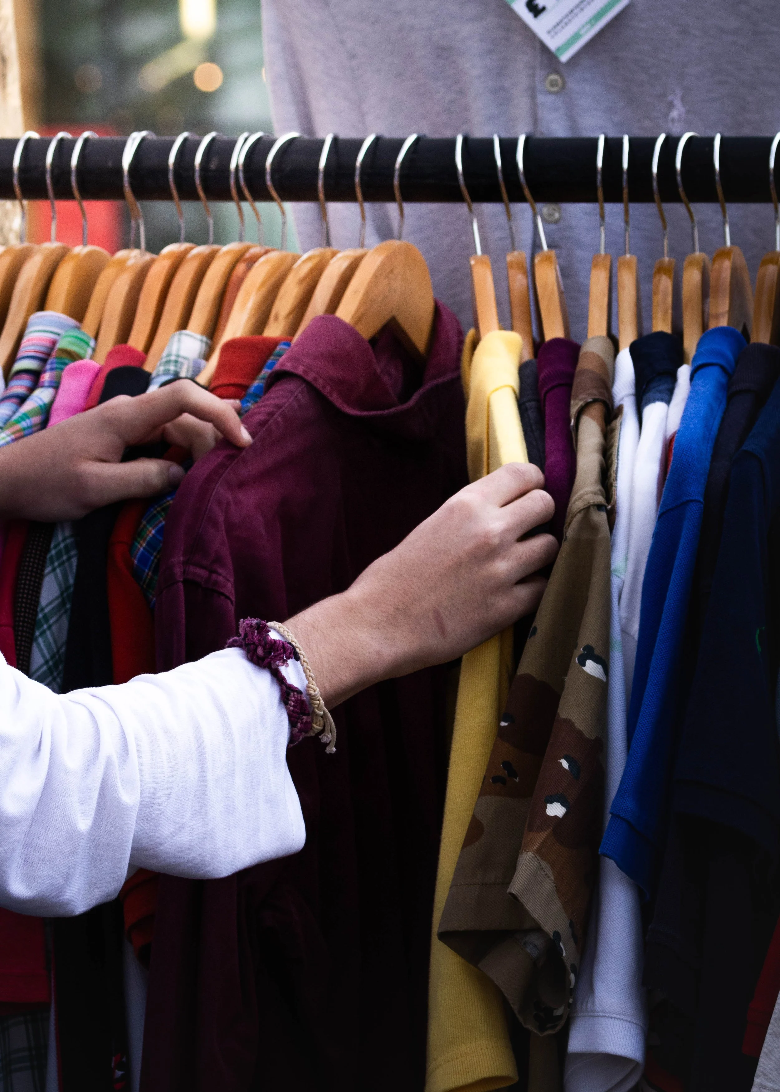 Person selecting colorful shirts on a clothing rack at a store.