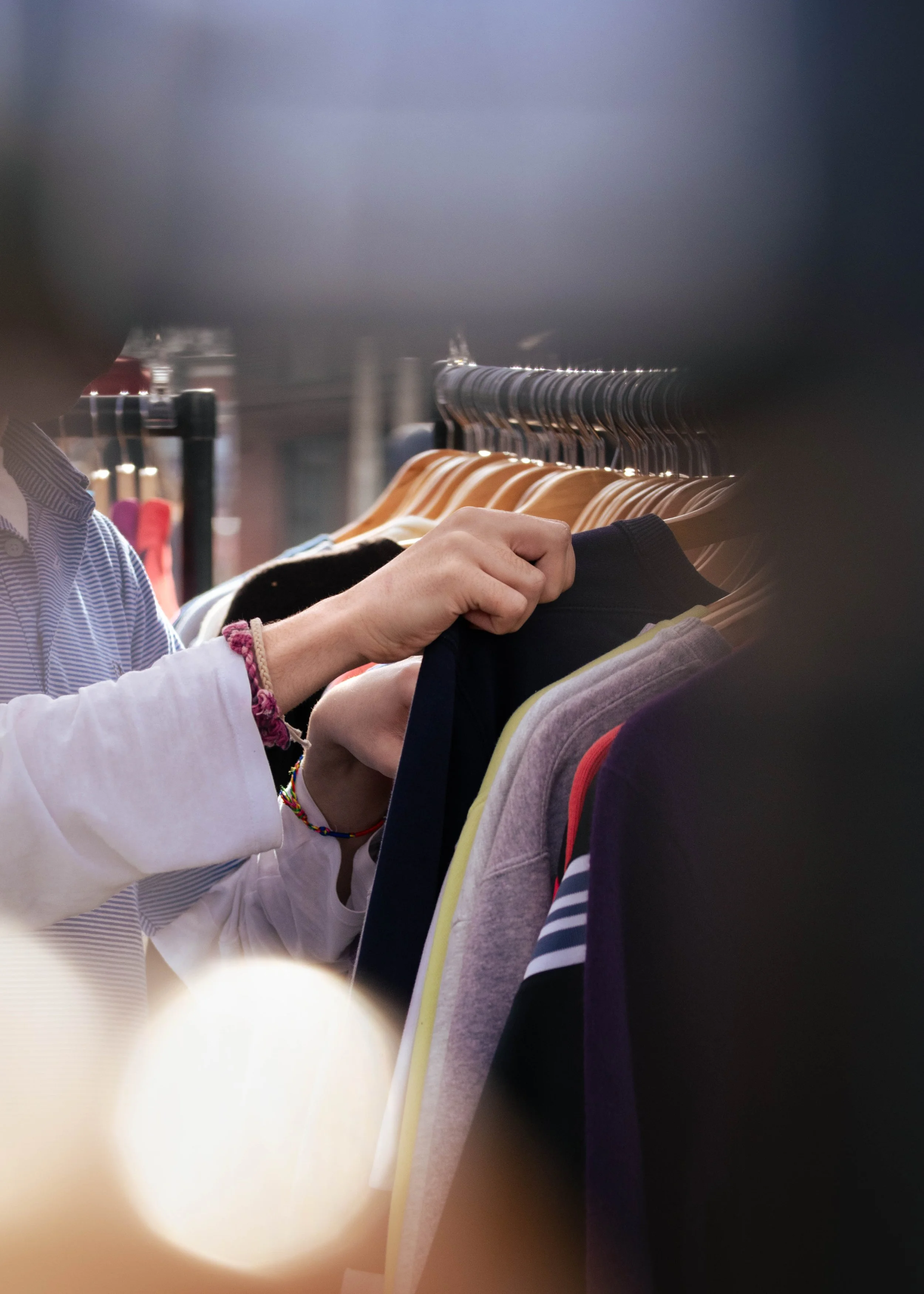 Person browsing through a clothing rack filled with various colored shirts.