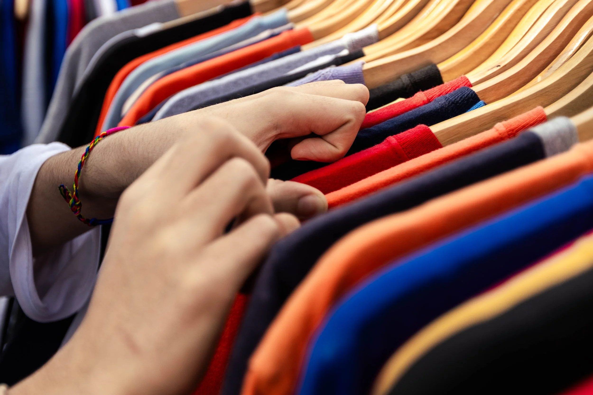 A person holding a clothing hanger with multiple shirts on it, in various colors including red, blue, black, gray, and orange.