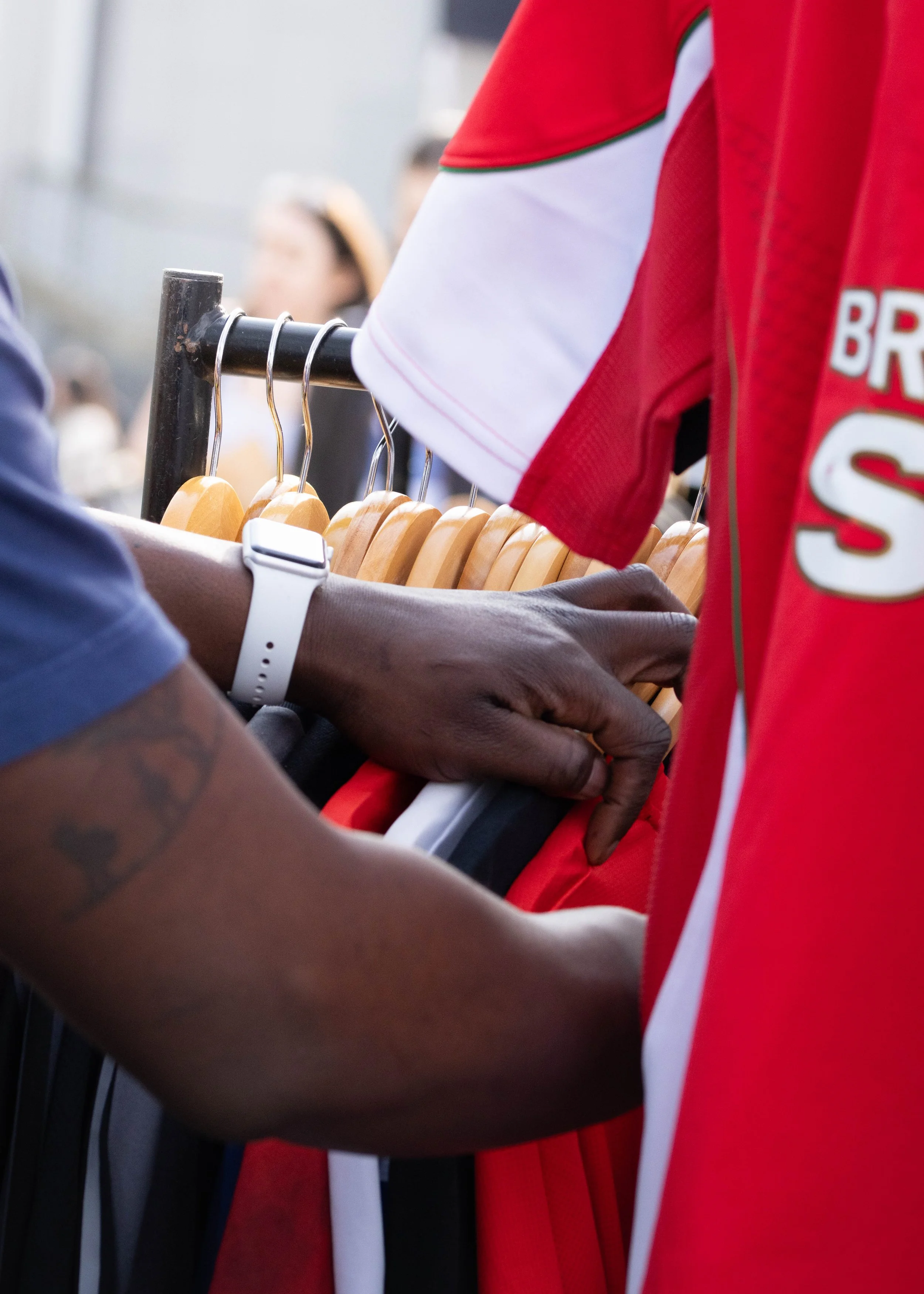 Close-up of people hanging their coats on a black coat rack, with one person wearing a red sports jersey and a white wristwatch.
