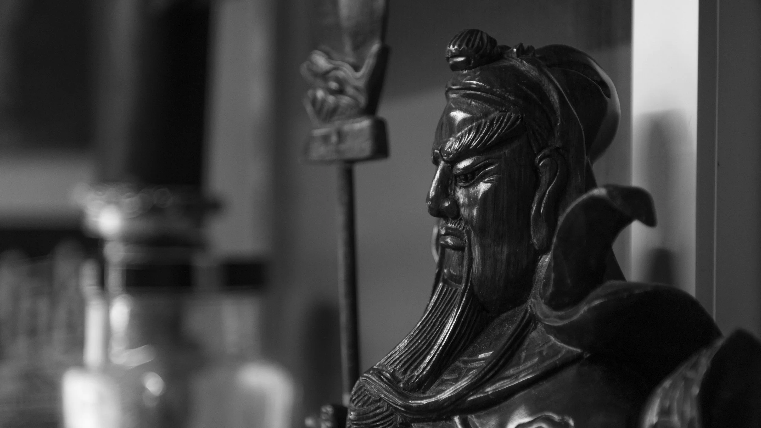 Black and white close-up of carved wooden bust of a man with a beard and turban, focused on face and upper shoulders.