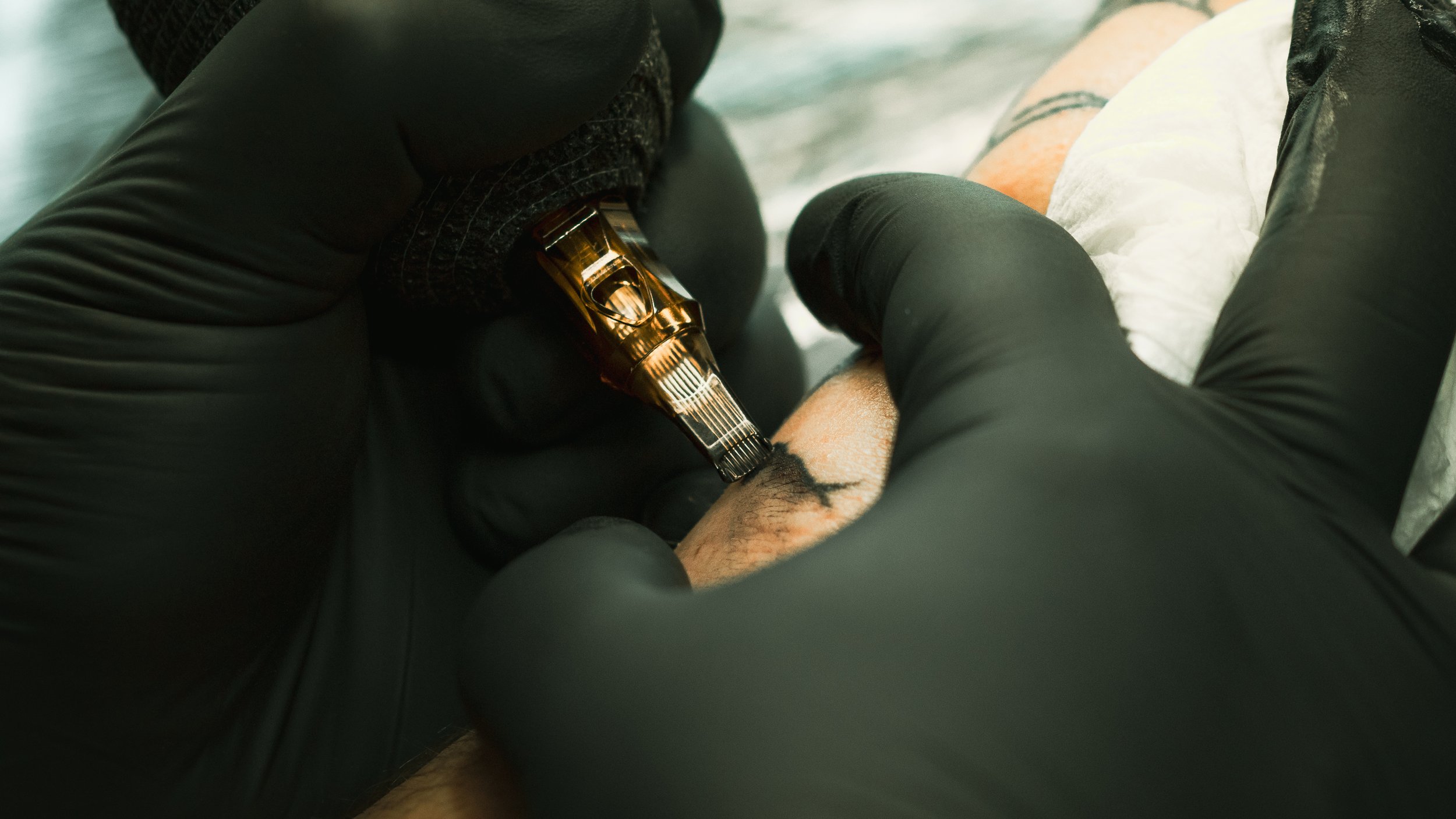 A person with black gloves tattooing skin with a tattoo machine.