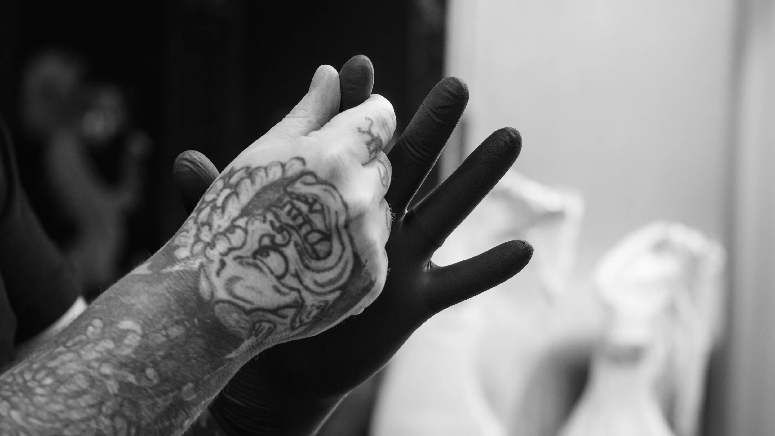 Close-up of two hands, one with detailed tattoos and the other wearing a glove, touching each other in a gentle gesture.