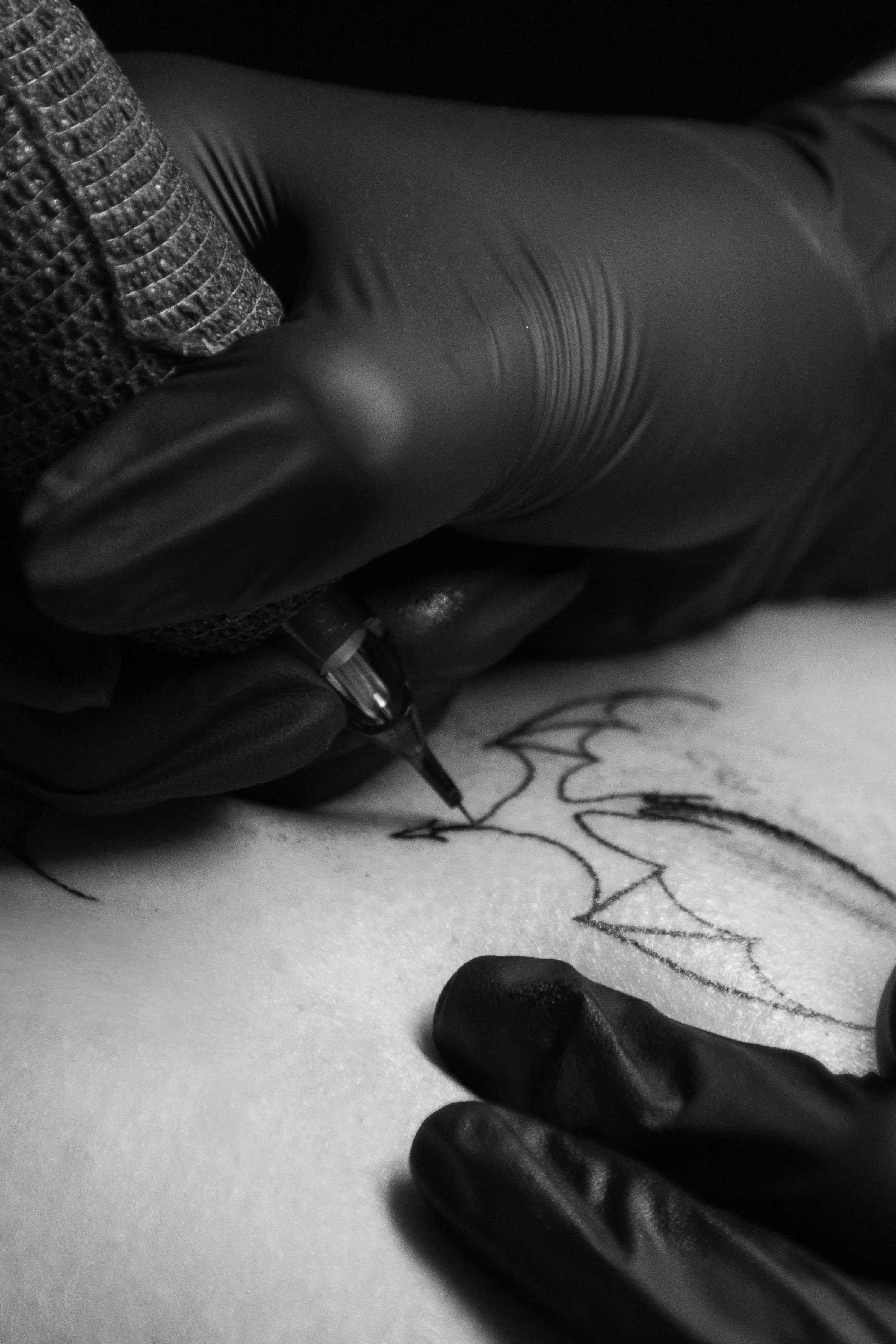 A person wearing black gloves is drawing a zigzag pattern on white paper with a pencil, with small black stones placed nearby.