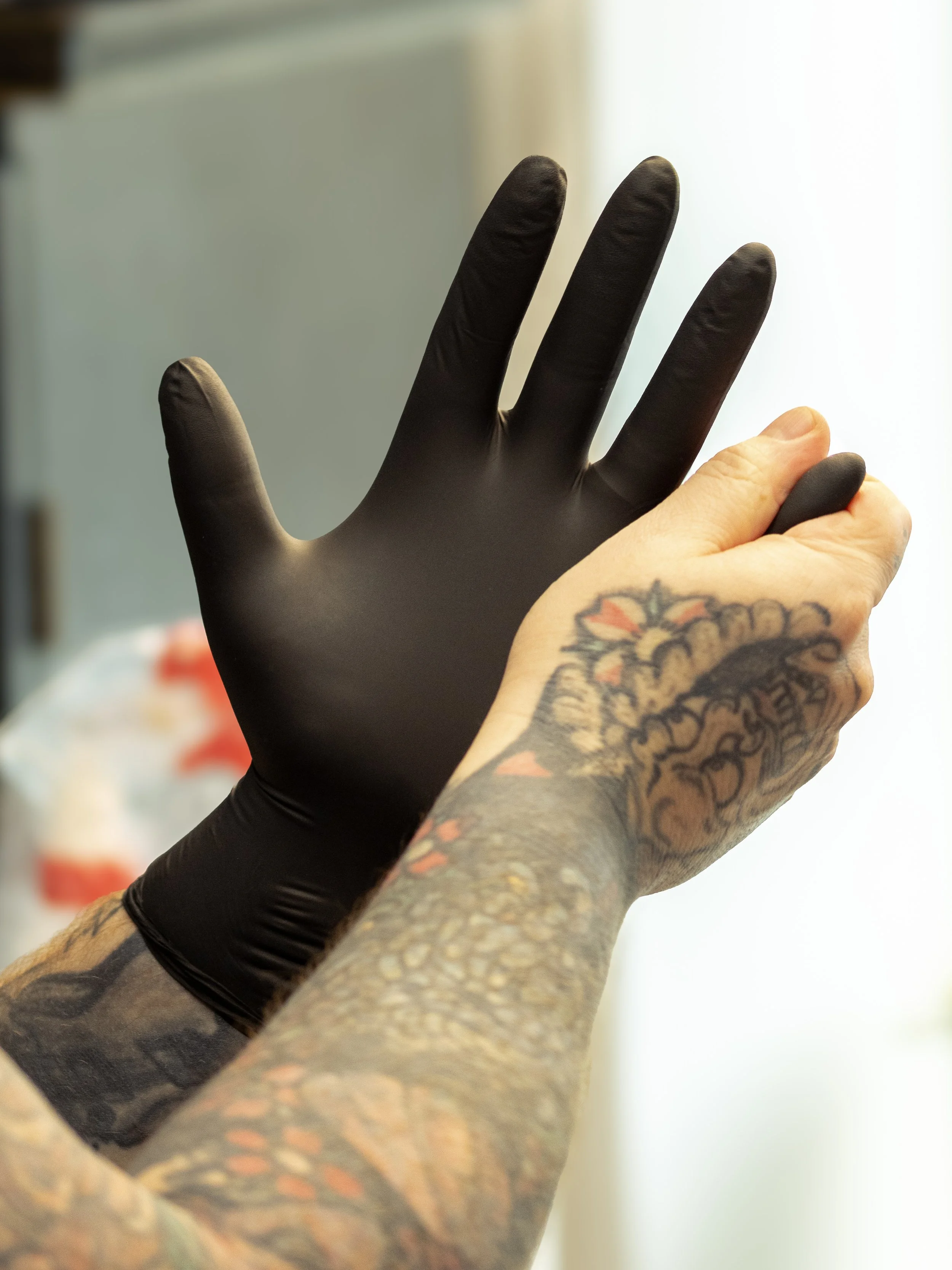 A person wearing a black glove, with tattoos on their arm, reaching towards a light source with their hand.