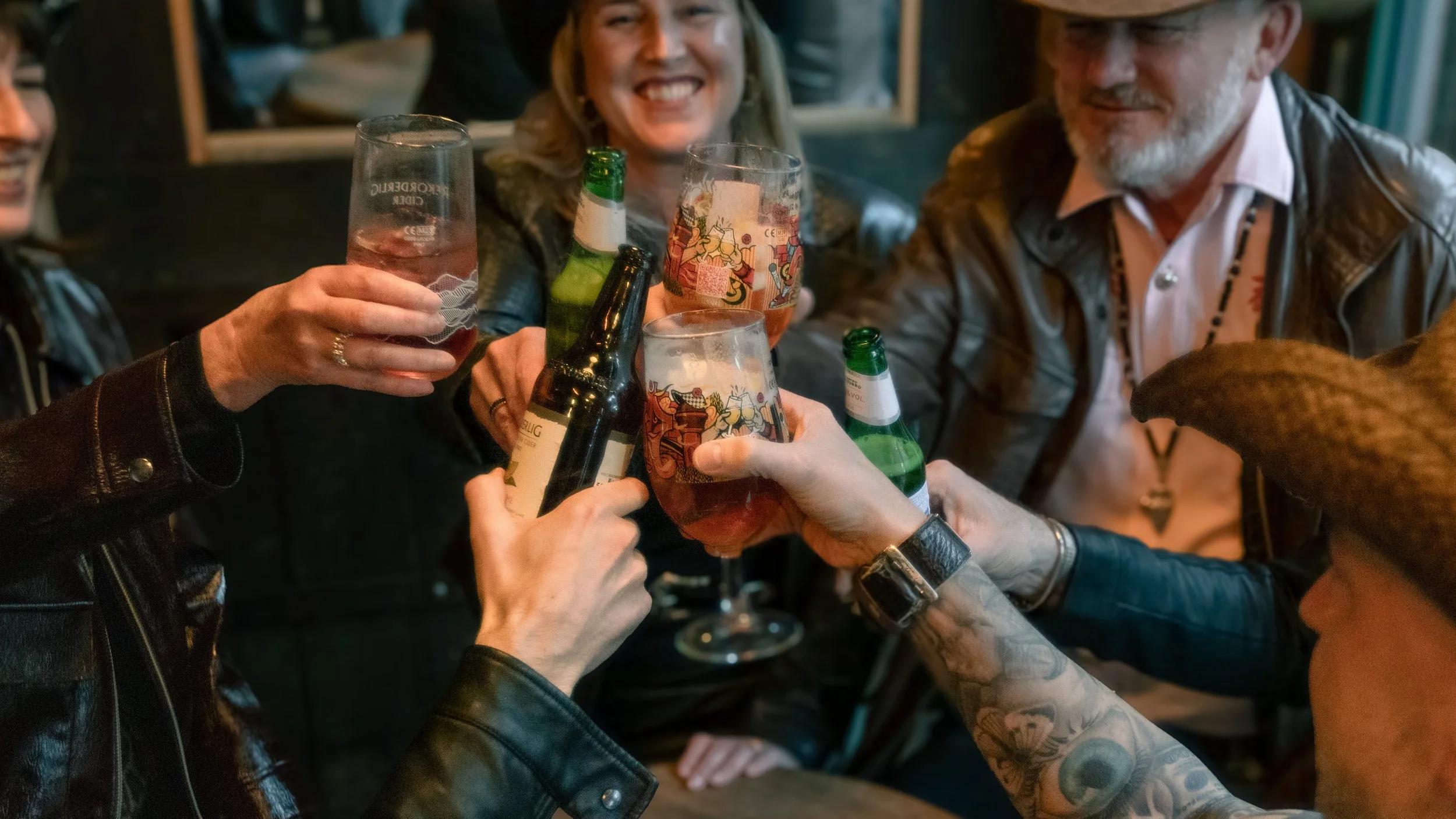 A group of friends raising glasses and bottles in a toast at a bar or pub, celebrating and smiling.