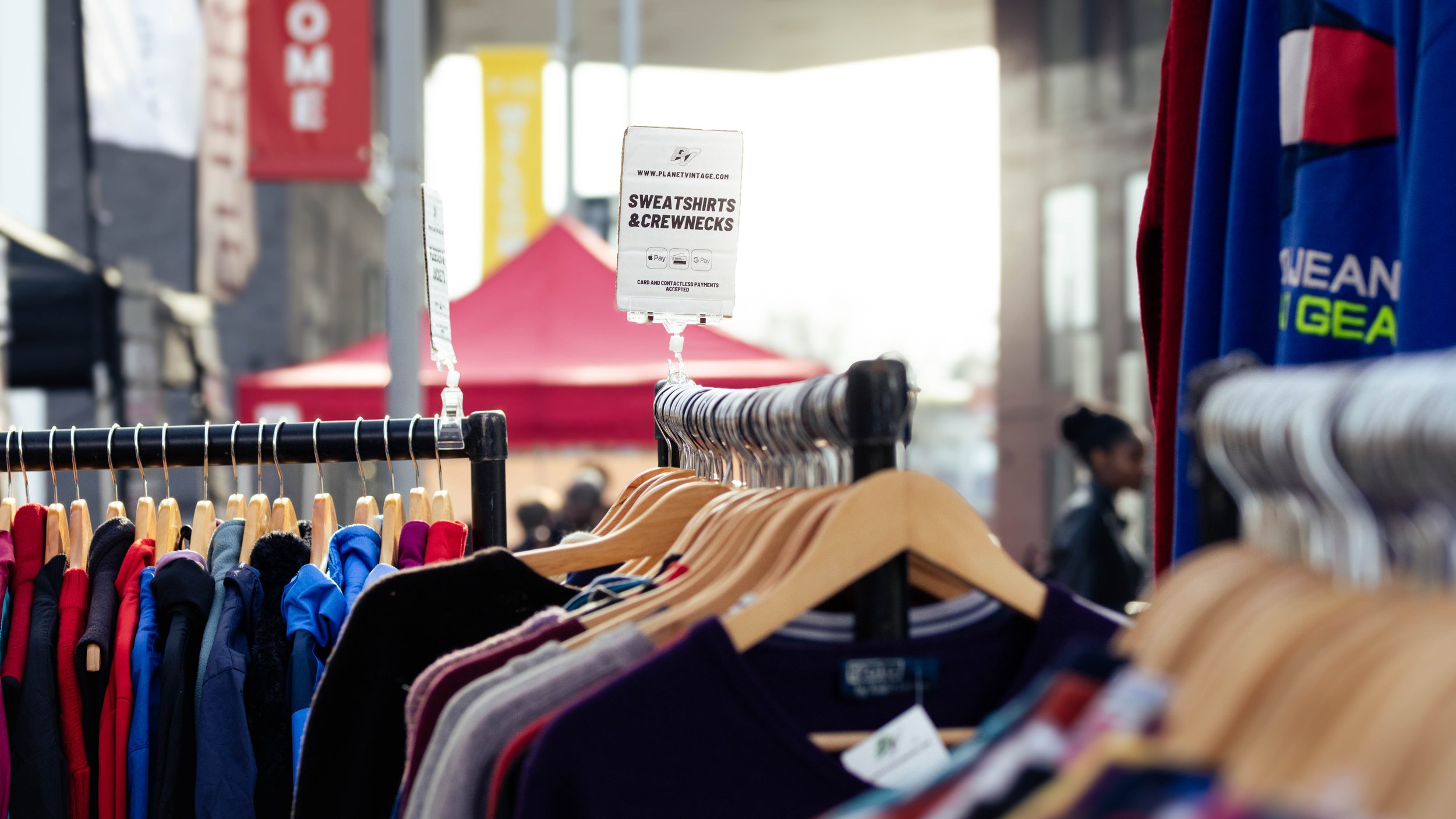Clothing rack with colorful sweatshirts, T-shirts, and crewnecks at an outdoor market.