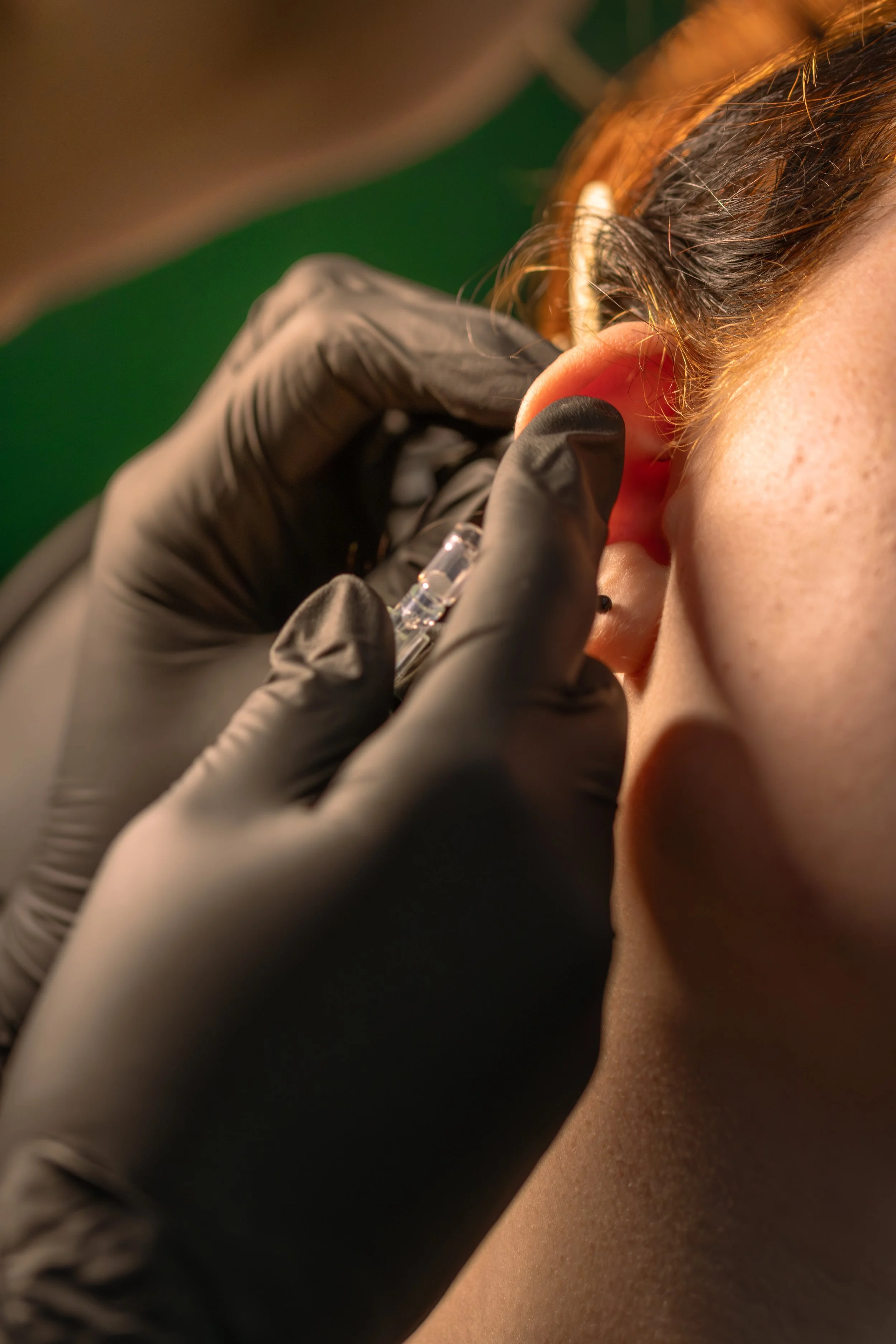Close-up of a person receiving a piercing in the earlobe, with a gloved hand holding the piercing needle.