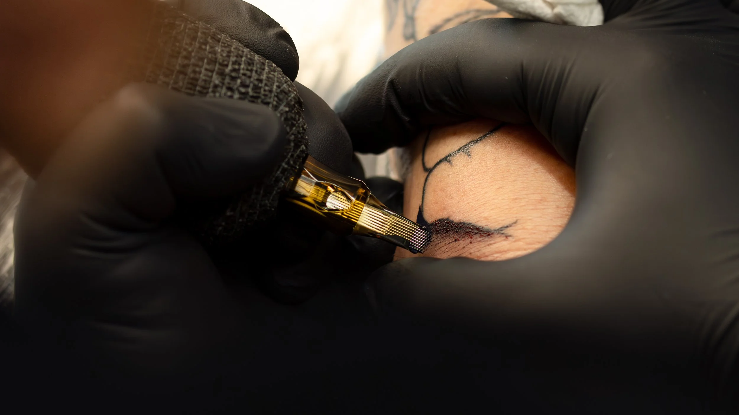 Close-up of a tattooing process, with a tattoo needle applying ink to skin, wearing black gloves.