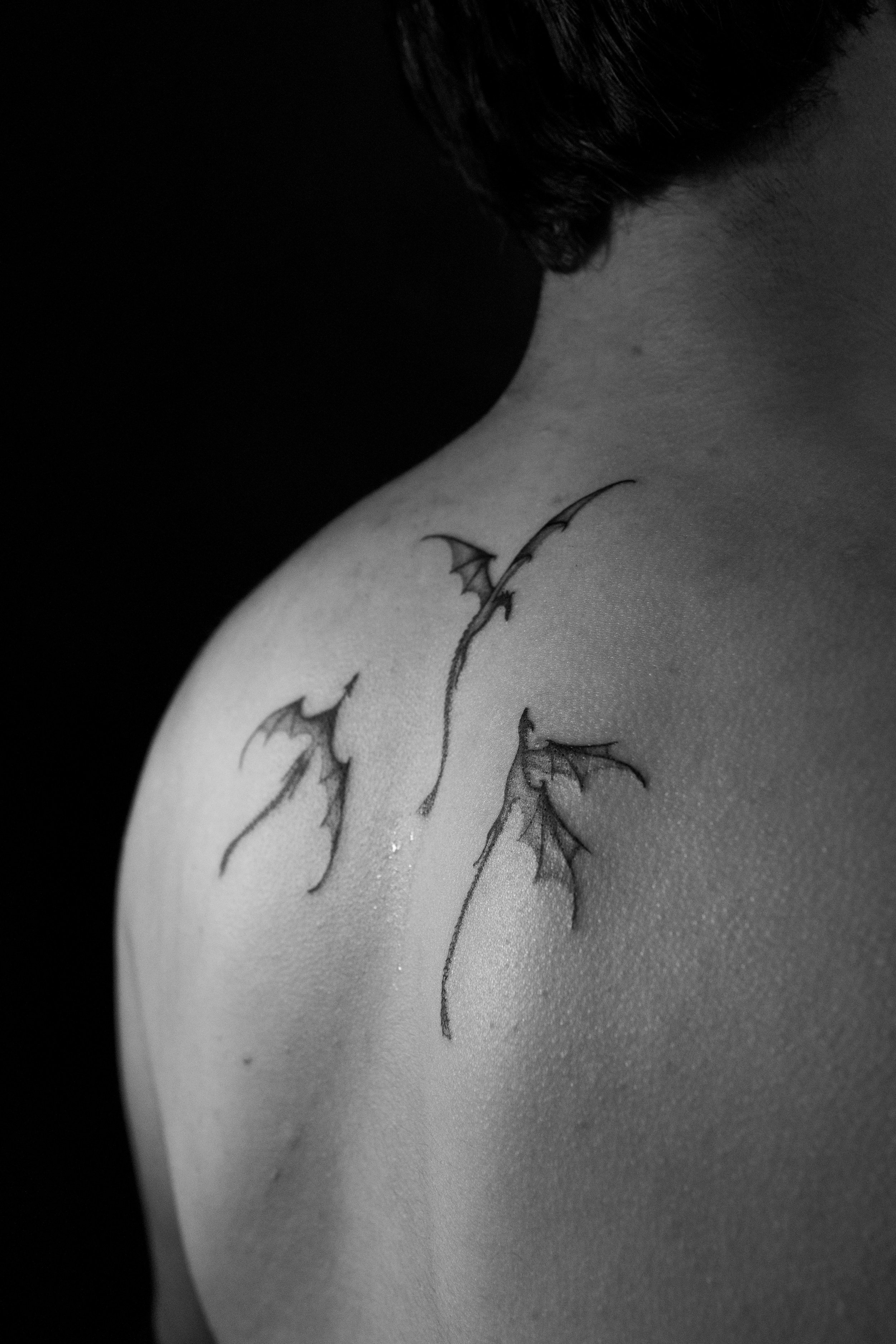 Close-up black and white photo of a person's shoulder with a tattoo of flying bats.