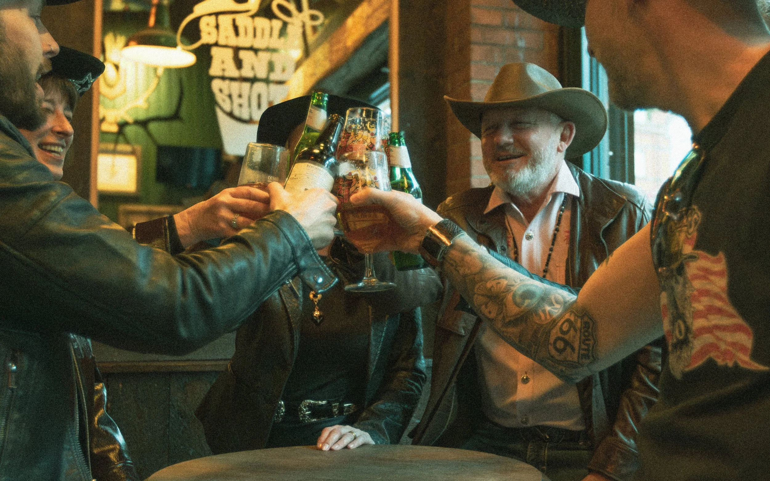 Group of friends gathered in a bar, clinking beer bottles and glasses for a toast, smiling and enjoying themselves.