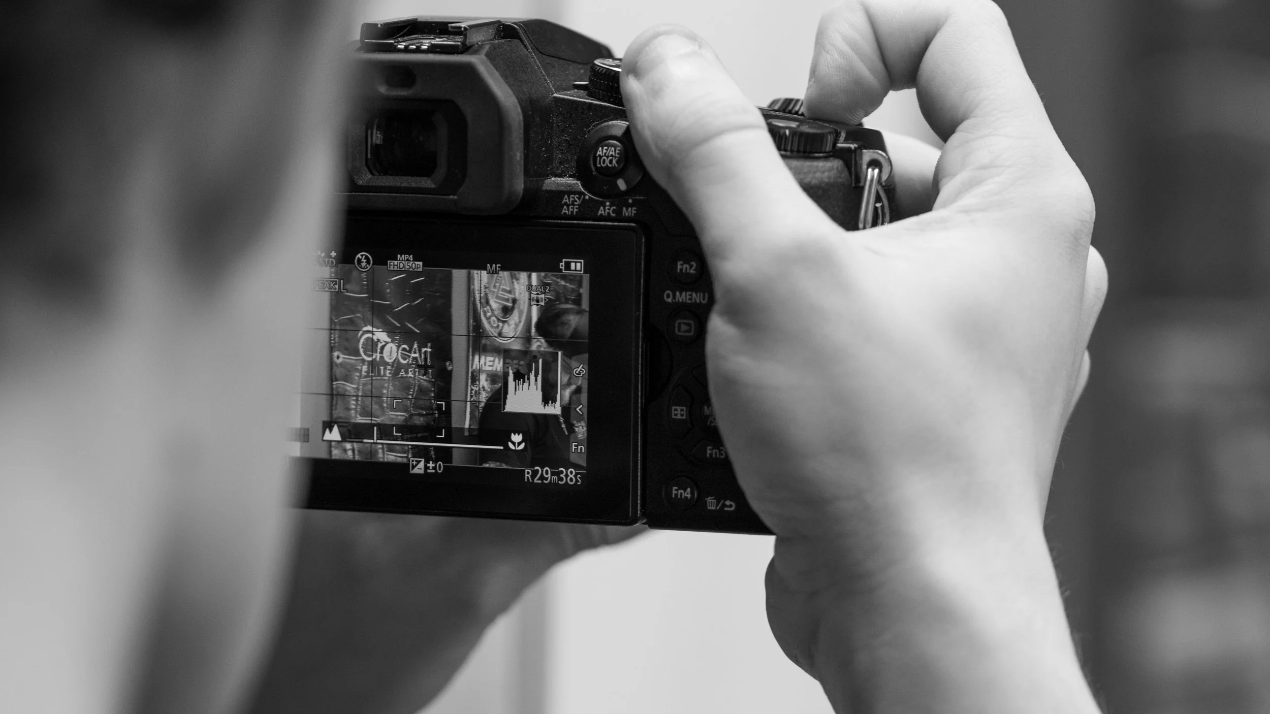 A person taking a photo with a digital camera, focusing on the camera's screen and controls, in black and white.