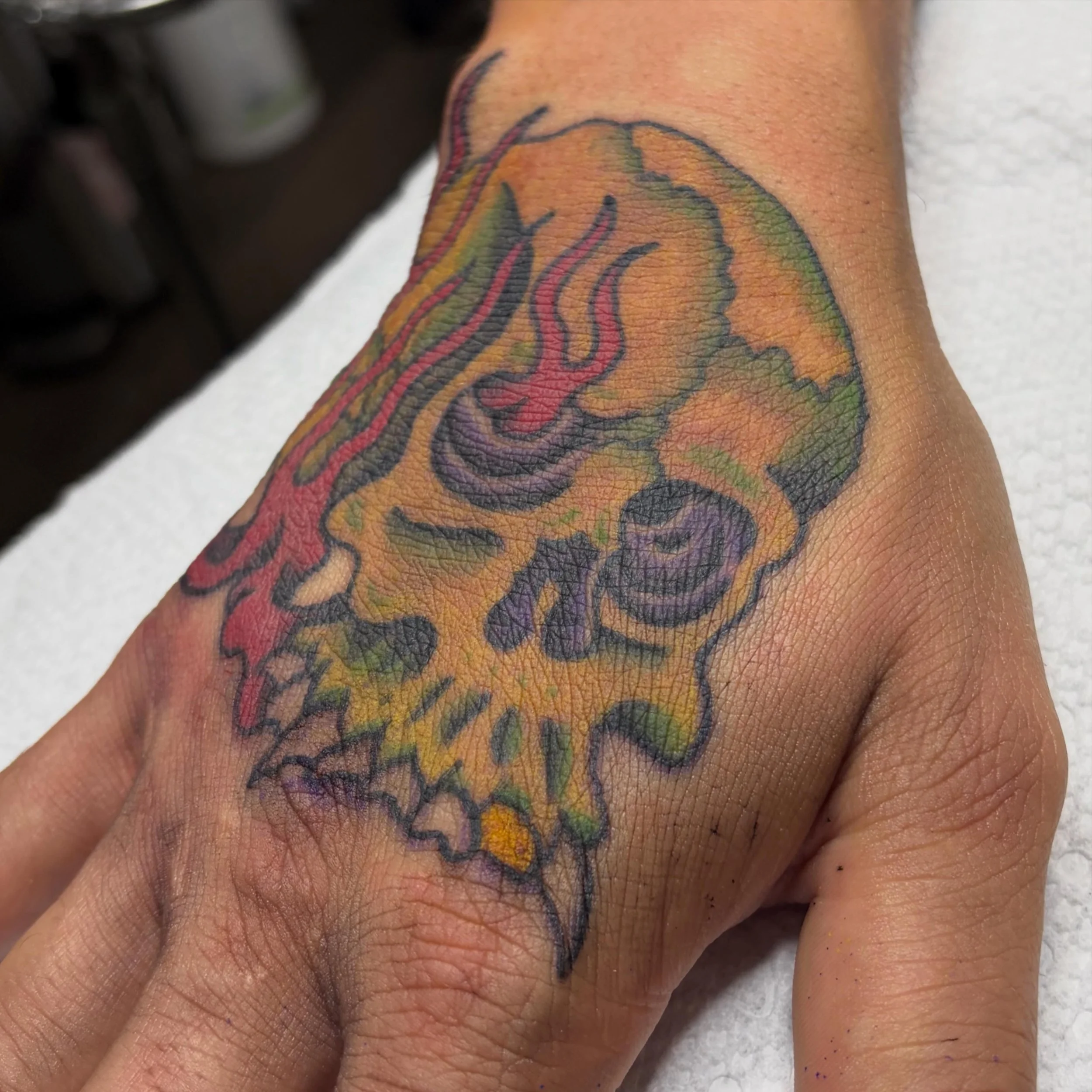 A colorful tattoo of an abstract design on a person's arm, featuring various shades of orange, green, purple, and black.