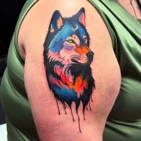 Colorful wolf tattoo on upper arm with abstract, dripping style.