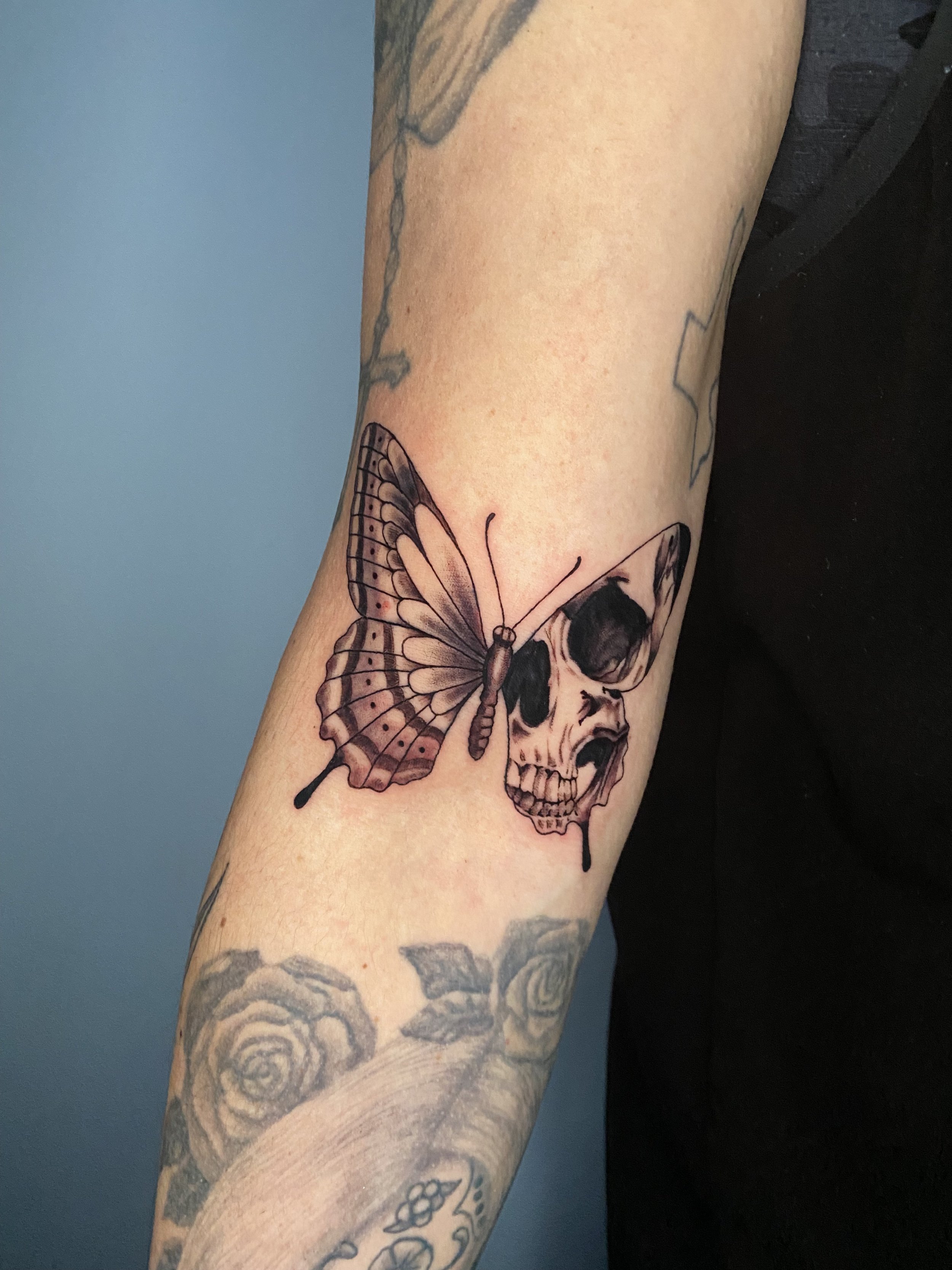 Tattoo of a butterfly and a skull on a person's forearm.
