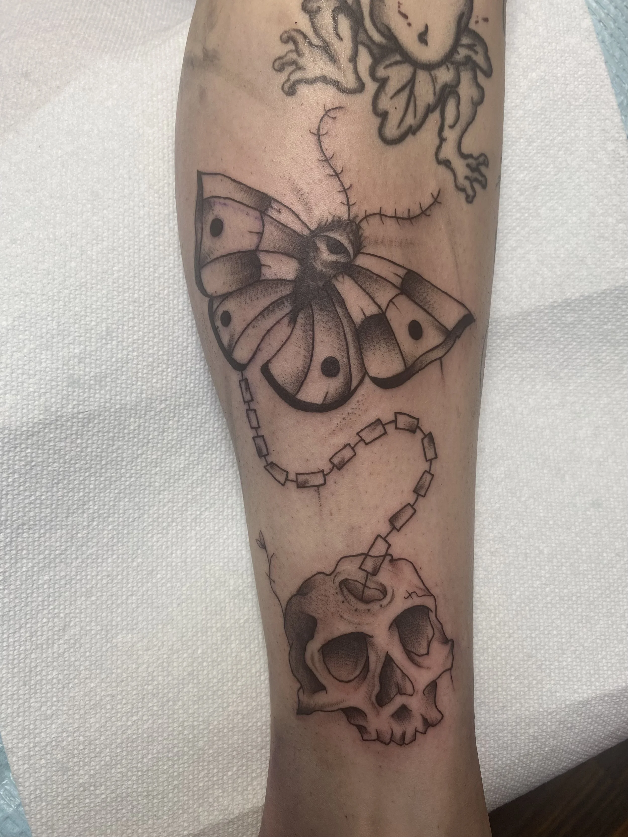 Tattoo of a butterfly flying above a human skull on a person's arm.